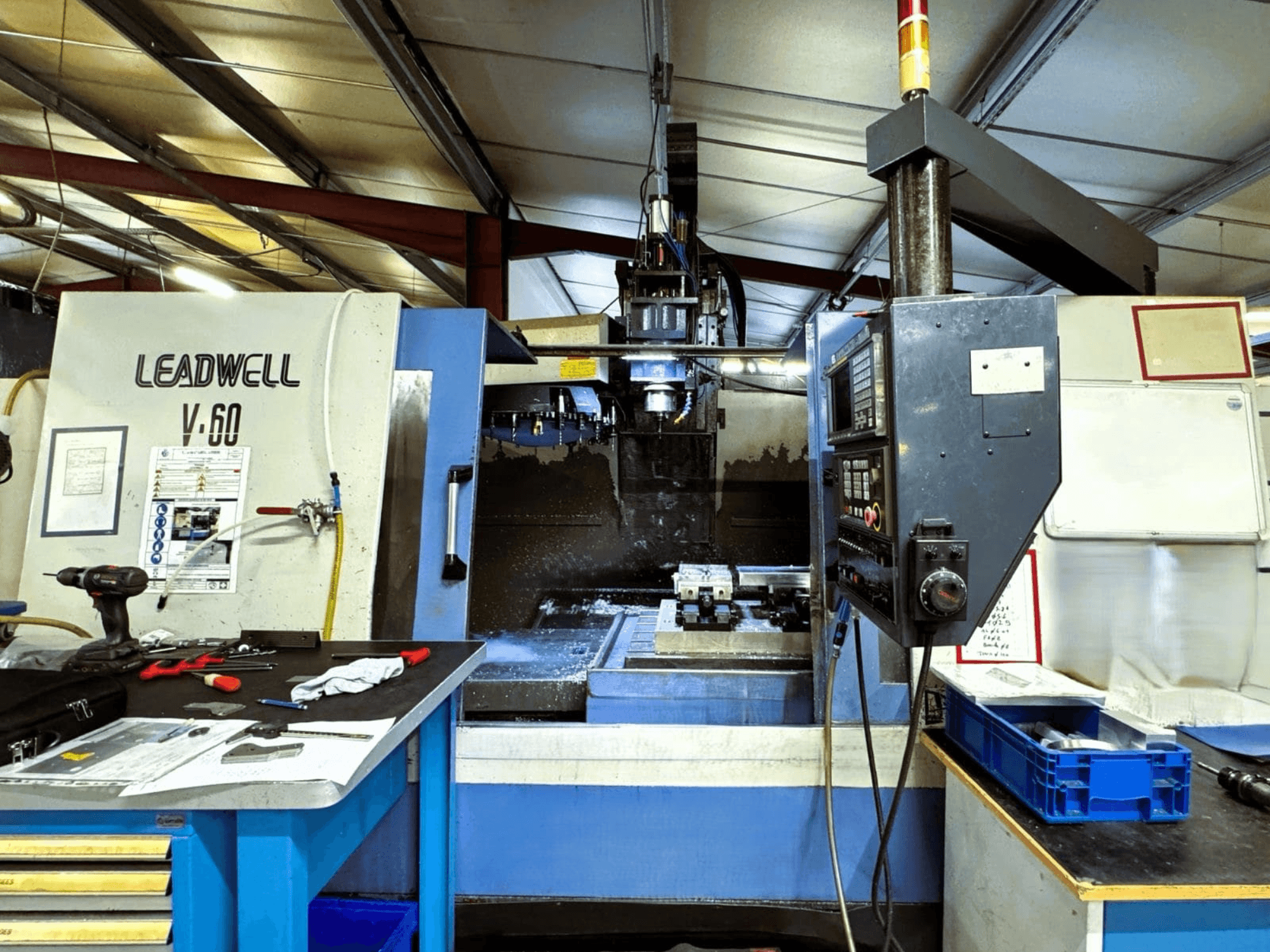 Centro de mecanizado vertical Leadwell V-60 visto de perfil, en el que se aprecian el panel de control y la zona de trabajo con herramientas y piezas.