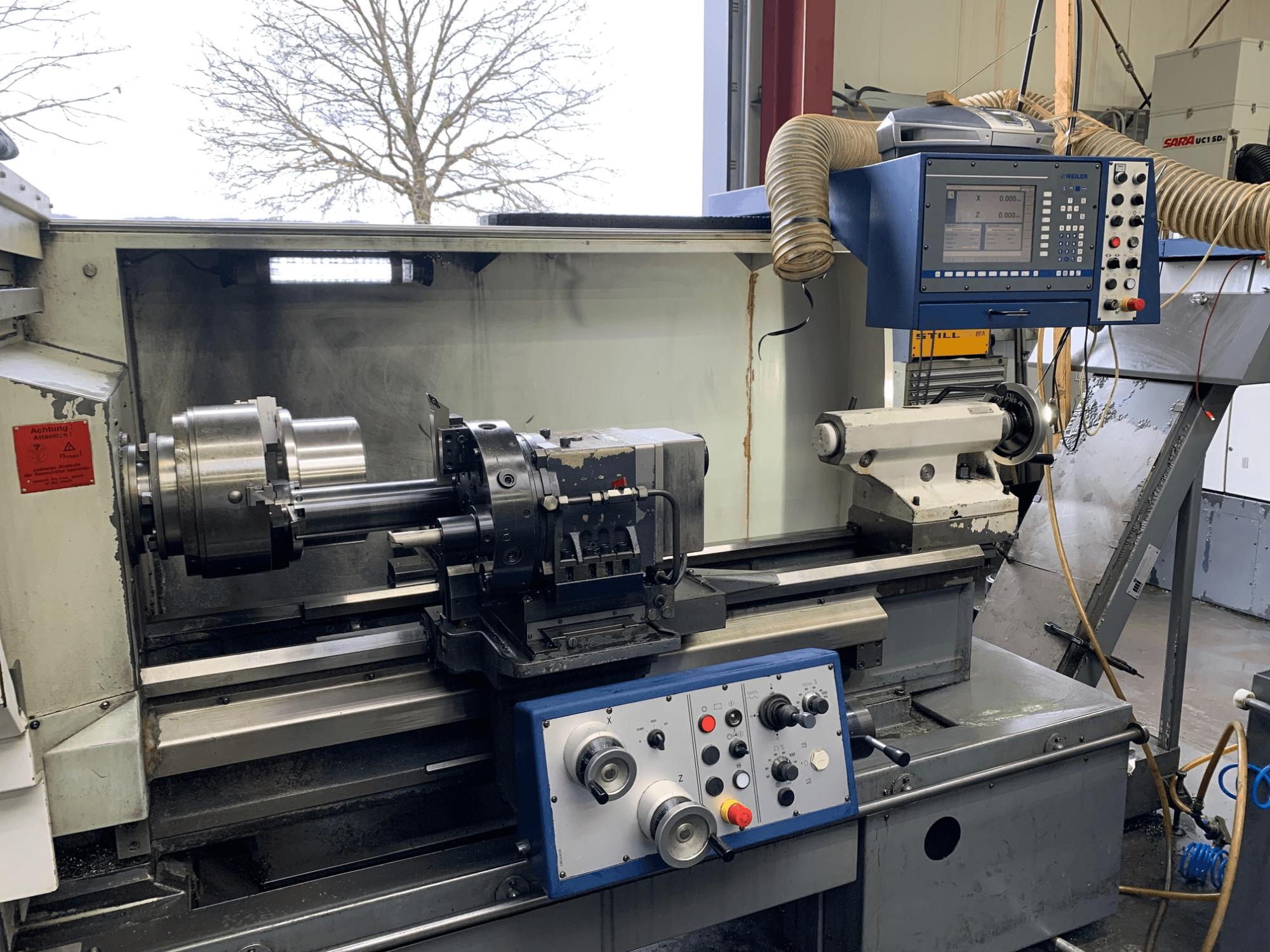 Máquina de torneado horizontal Weiler E55X1000 en un taller, mostrando el panel de control, el torno y el portaherramientas. Vista frontal.