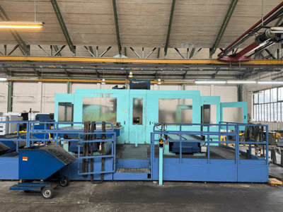 Máquina CNC industrial azul con paneles protectores, vista frontal, con almacenamiento de herramientas y un carro de recogida de residuos en el lateral.