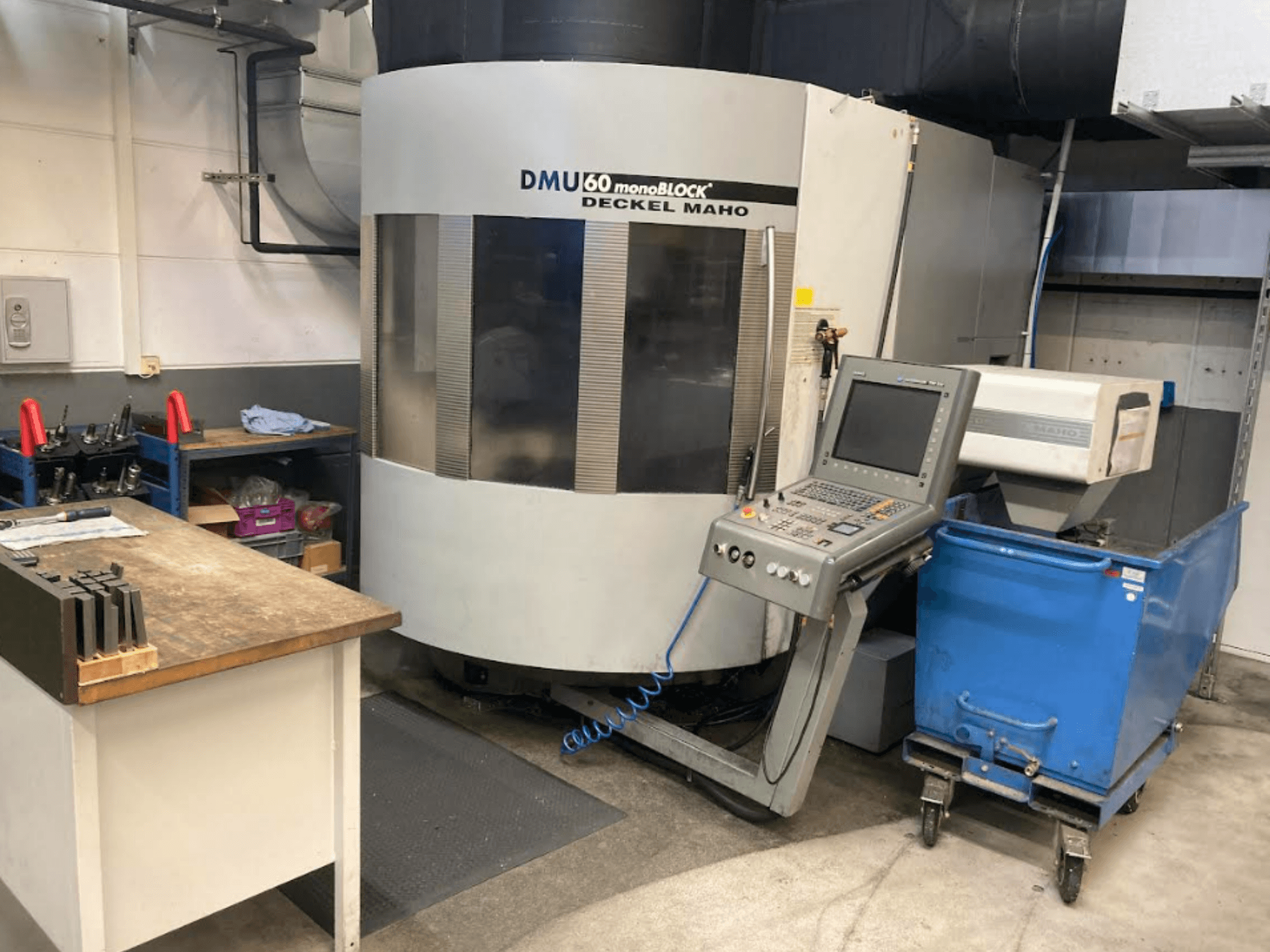 Centro de mecanizado vertical DMG MORI DMU 60 Monoblock, vista frontal con panel de control, espacio de trabajo y carro de herramientas azul visible.