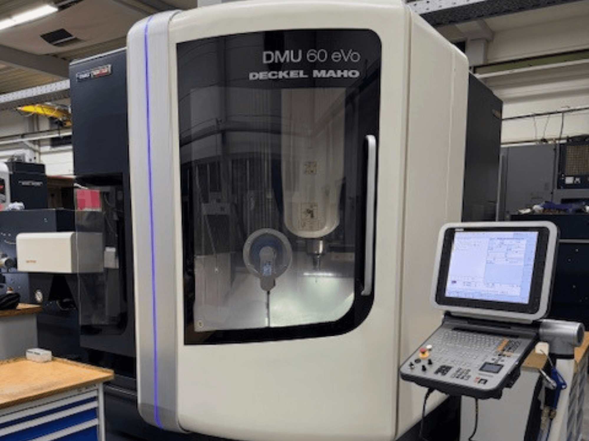 DMU 60 eVo de DECKEL MAHO, vista frontal de fresadora CNC con panel de control y pantalla de visualización, mostrando componentes de precisión.