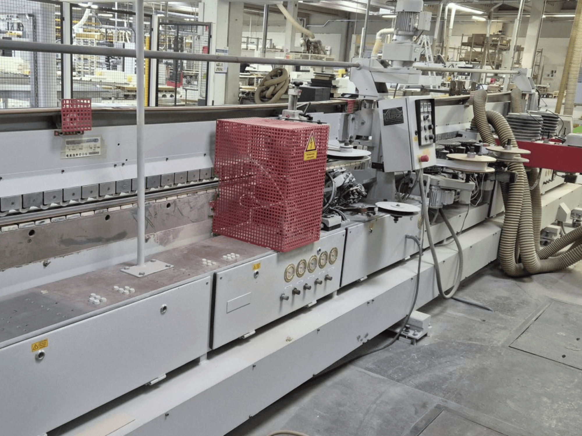 Encoladora de cantos con panel de control, mangueras de aspiración y cubierta de seguridad roja, vista desde un ángulo lateral.