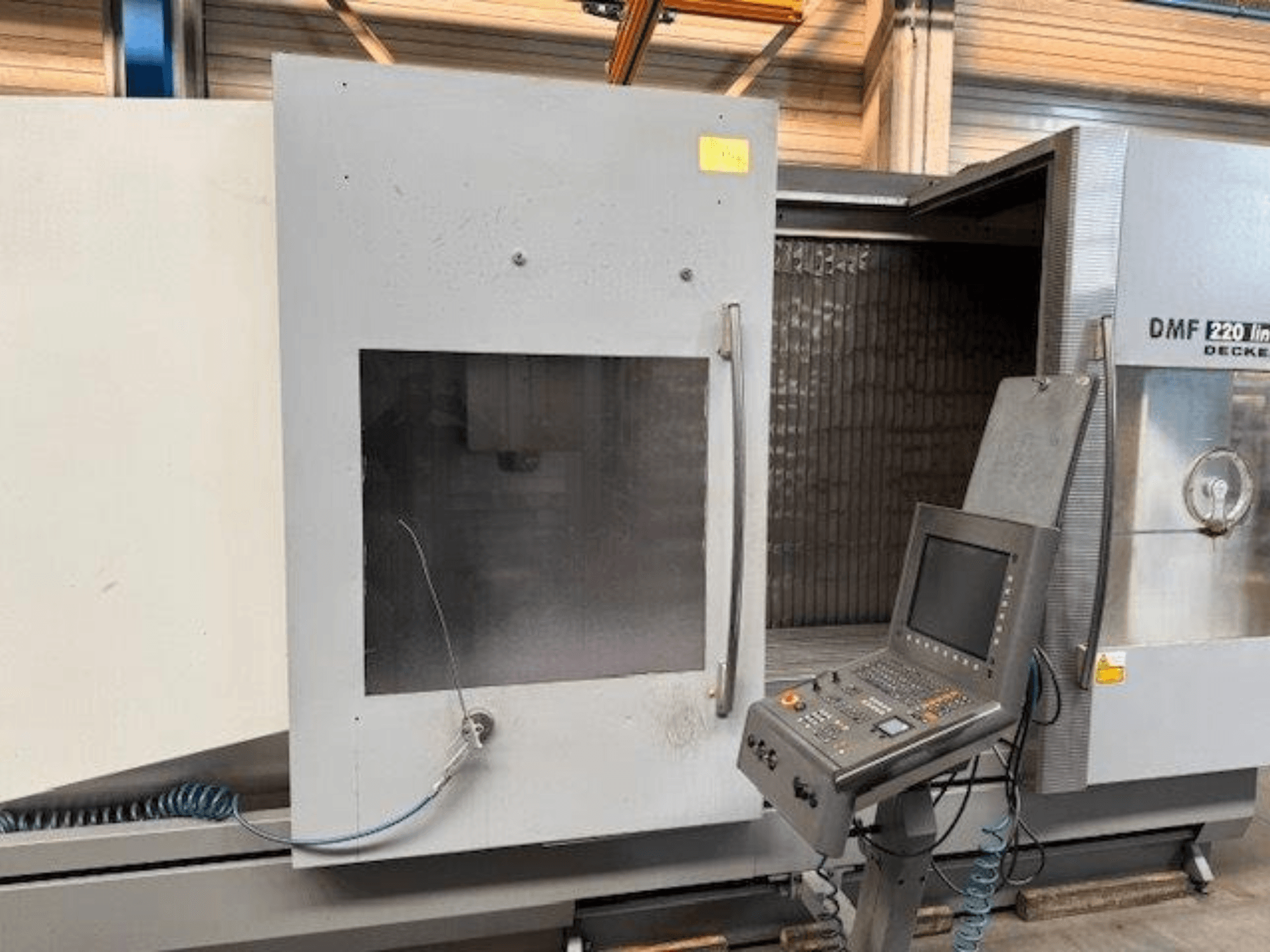 Vista frontal del centro de mecanizado vertical lineal DECKEL MAHO DMF 220, mostrando el panel de control y la puerta de la máquina abierta.