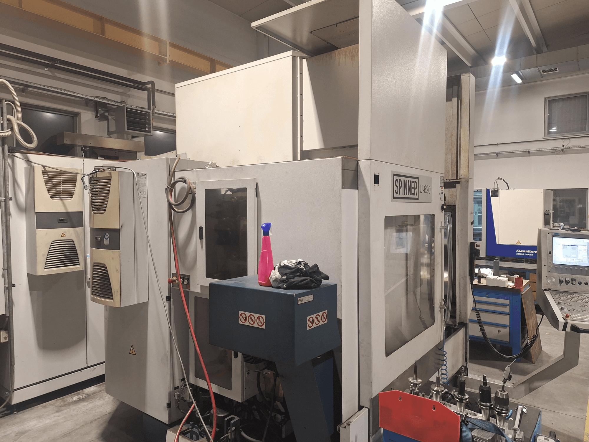 Máquina CNC Spinner U-620 mostrada desde una vista frontal en un taller, con panel de control y varias herramientas en un banco de trabajo cercano.