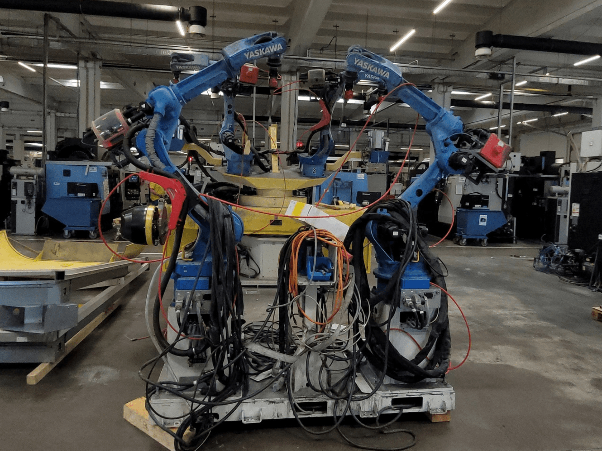 Célula de soldadura robótica Yaskawa RWC L1_OS 15330, vista frontal, con dos robots azules equipados con cables de gran longitud y herramientas de soldadura.