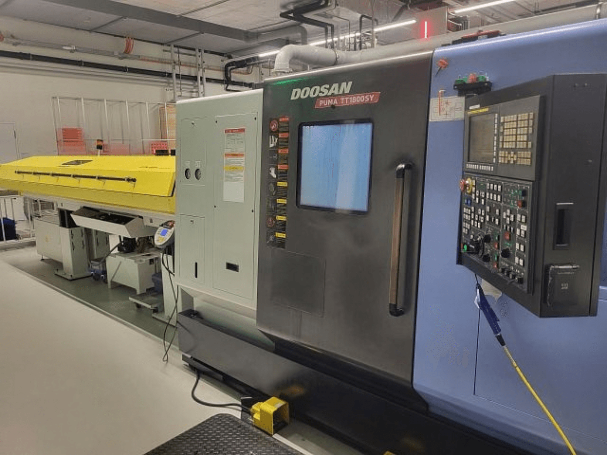 Centro de torneado y fresado DOOSAN PUMA TT 1800 SY, vista frontal con panel de control y cubierta amarilla, entorno industrial.
