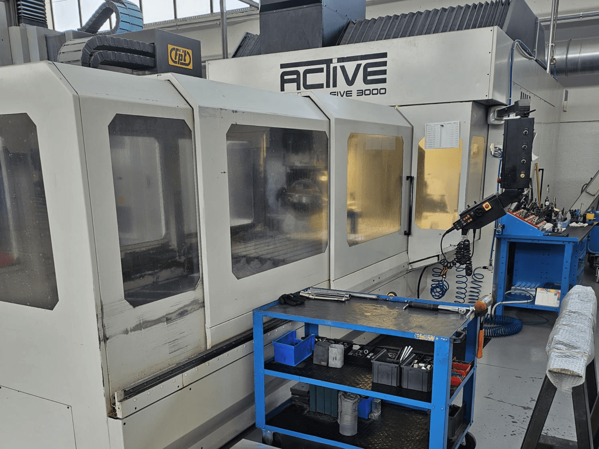 Máquina CNC Active 3000 en un taller, vista frontal con herramientas en un carro azul, controles visibles y área de trabajo en el interior.