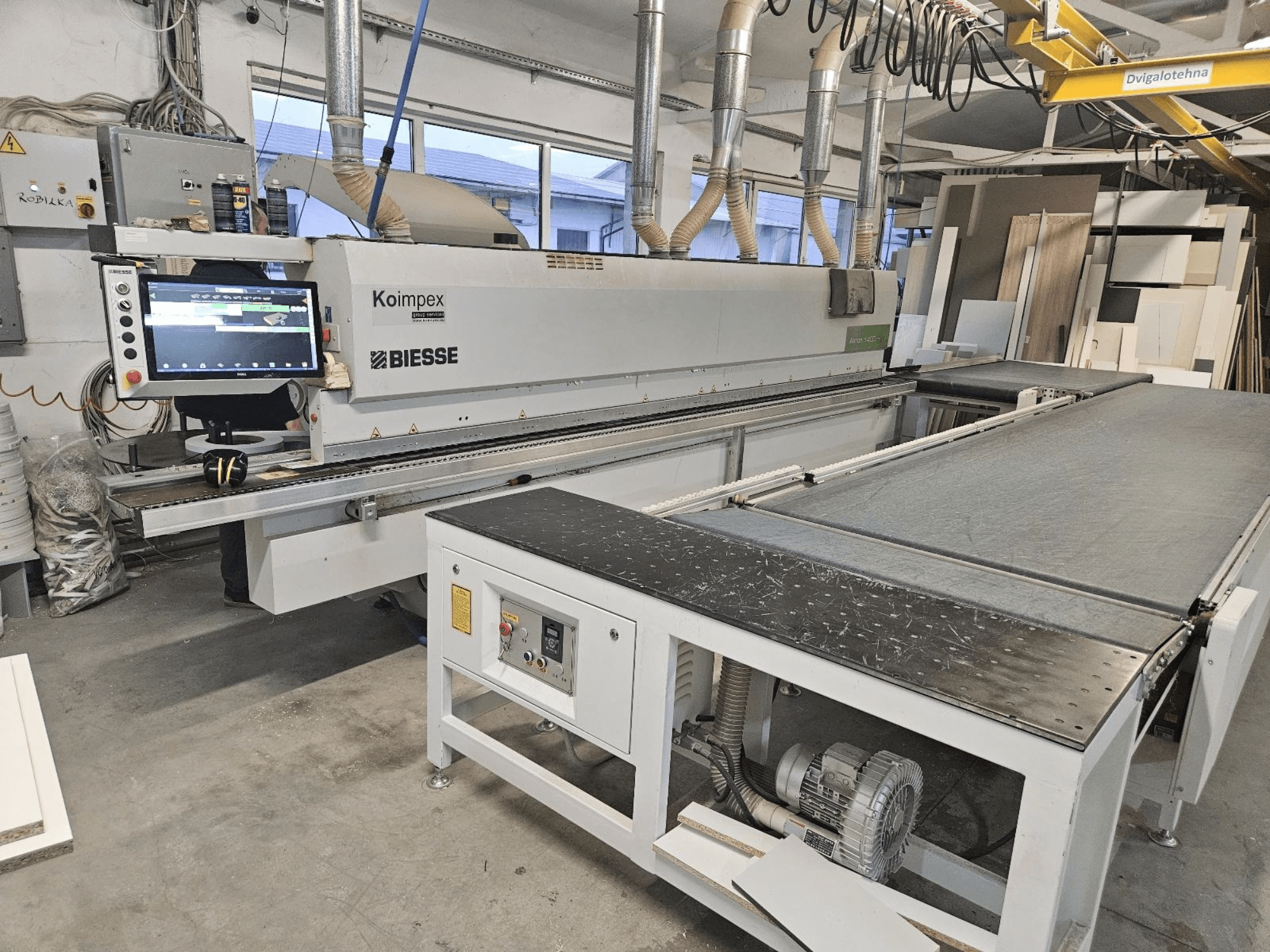 BIESSE Akron 1440 Una chapadora de cantos en un taller, vista lateral mostrando el panel de control y la cinta transportadora.