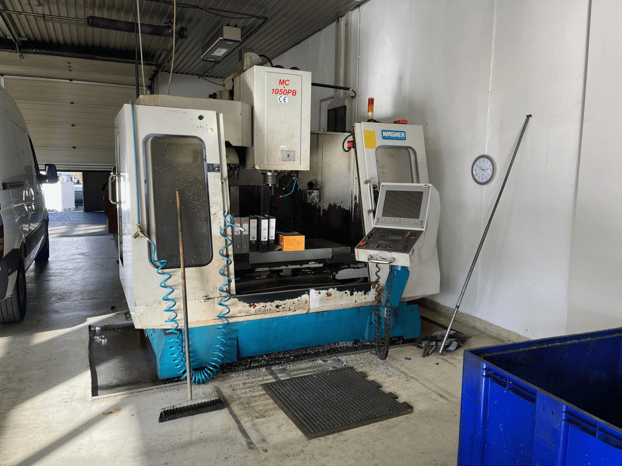 Máquina CNC WAGNER MC 1050PB en taller, vista frontal, con panel de control y área de trabajo; manguera de aire azul y herramientas de limpieza visibles.