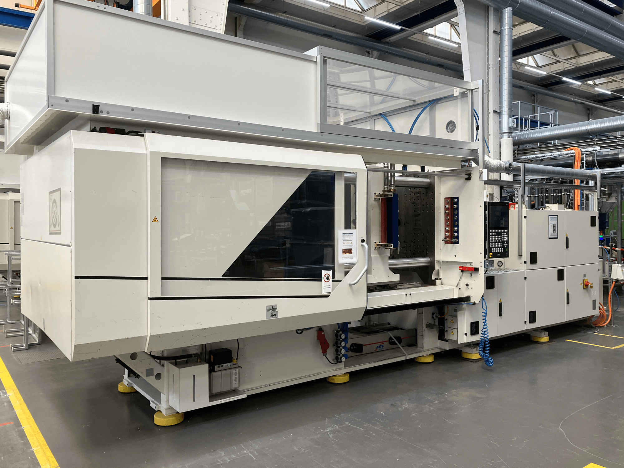 Vista lateral de una máquina de moldeo por inyección, modelo AET, con panel de control y cubiertas transparentes, en un entorno industrial.