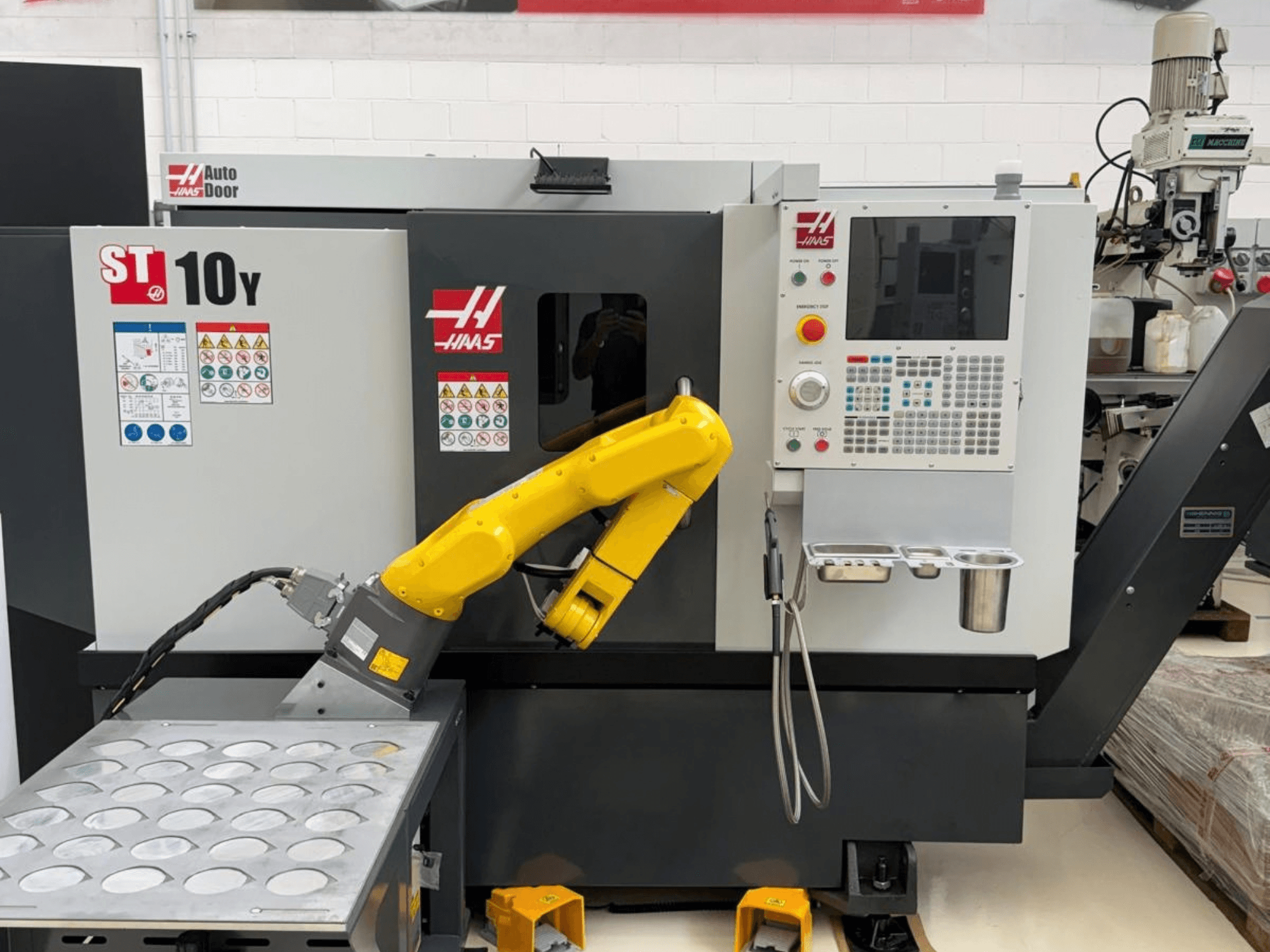 Torno horizontal Haas ST-10Y visto desde delante, equipado con un brazo robótico y un panel de control con bandejas portaherramientas.