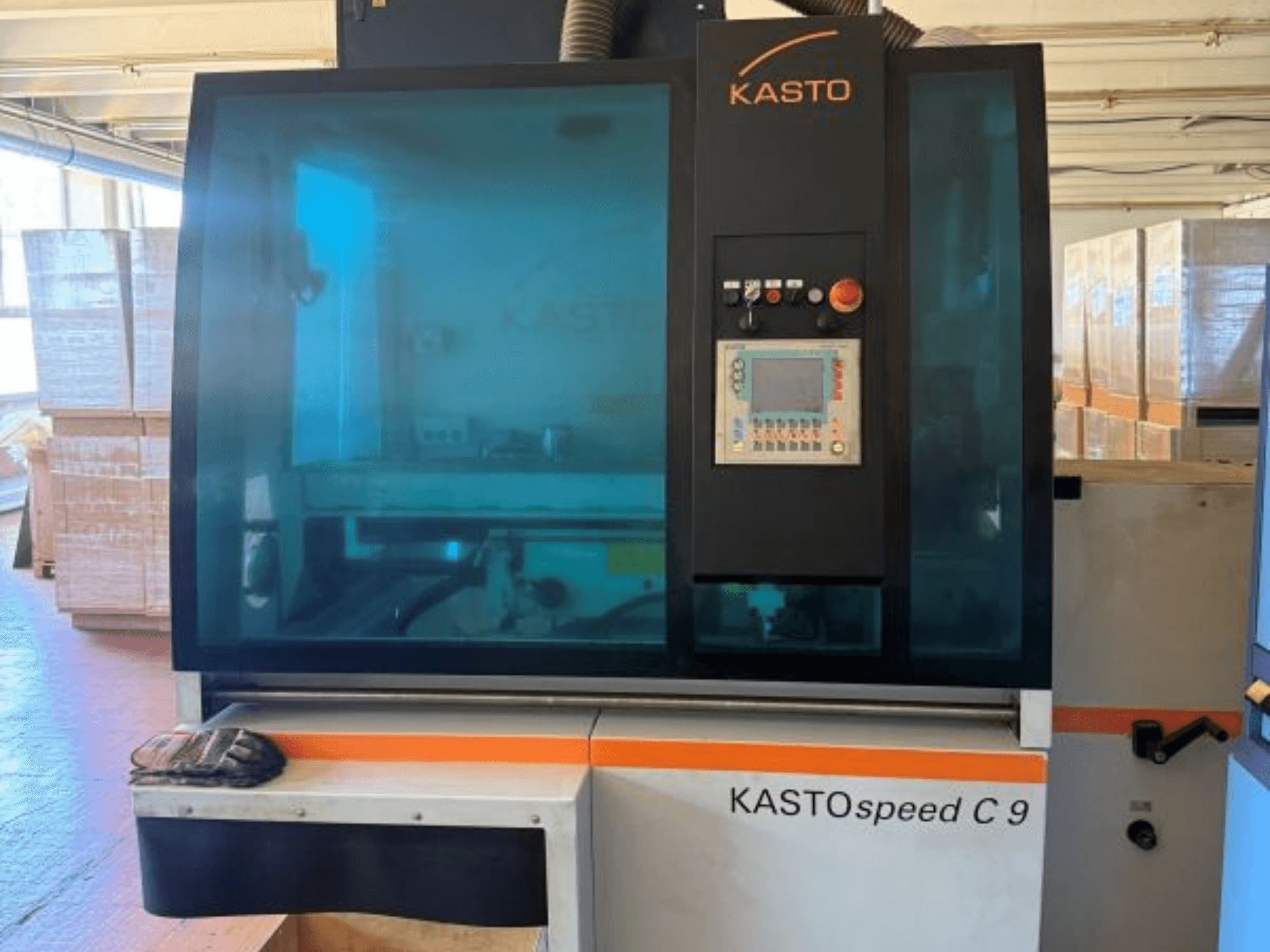Vista frontal de la sierra circular para metal KASTO KASTOspeed C 9, con el panel de control y el cristal de seguridad, y con cajas de madera al fondo.