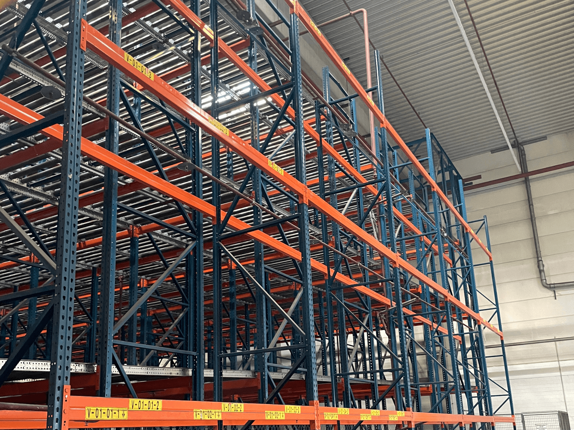 FL SYSTEME F05.10 Sistema de manipulación de paletas FLG en un almacén, mostrado desde una vista lateral, con estanterías para cargas pesadas de color naranja y azul.