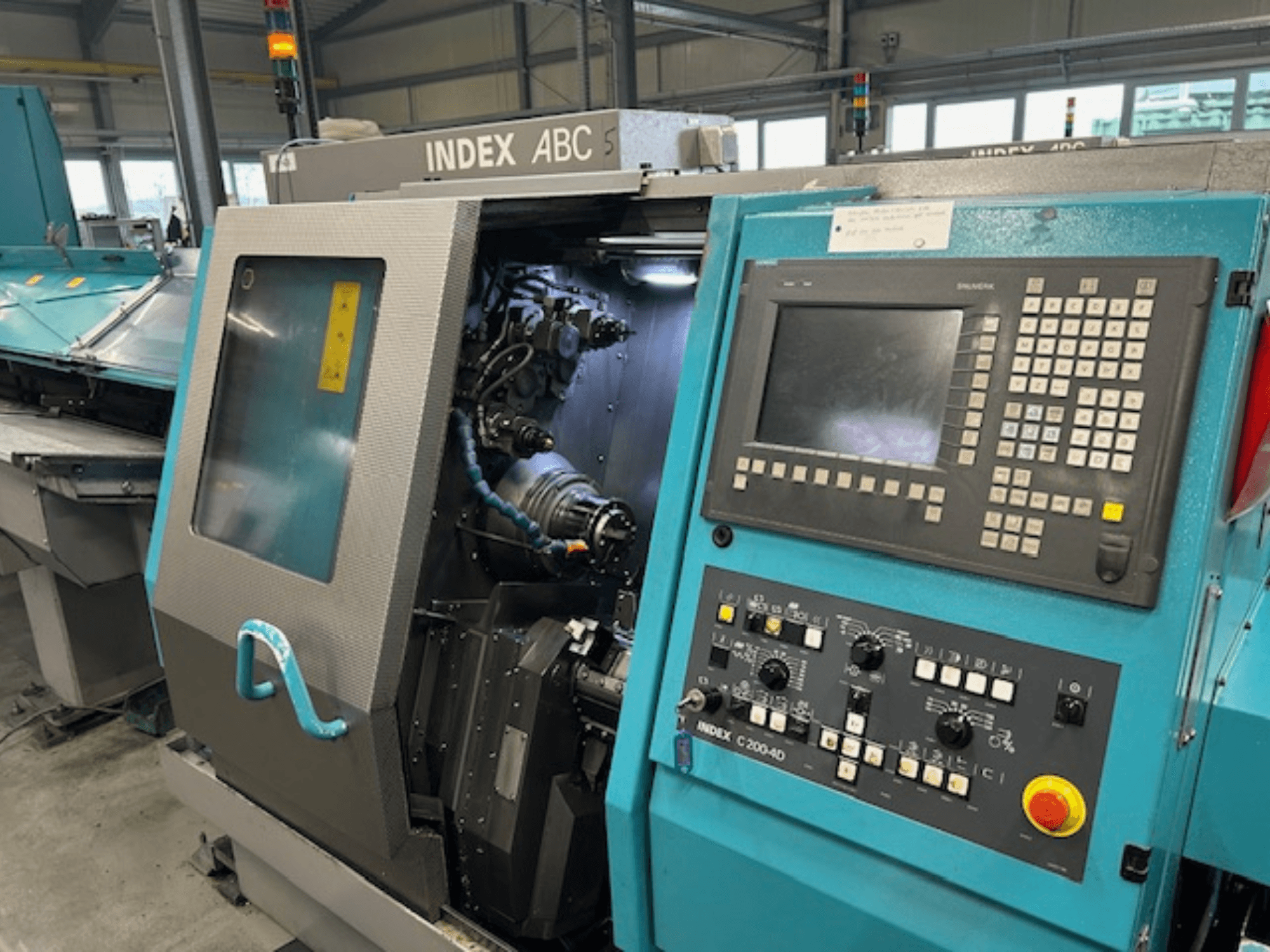 Vista frontal de un torno CNC INDEX C200-AD con panel de control, componentes internos visibles y características de seguridad.
