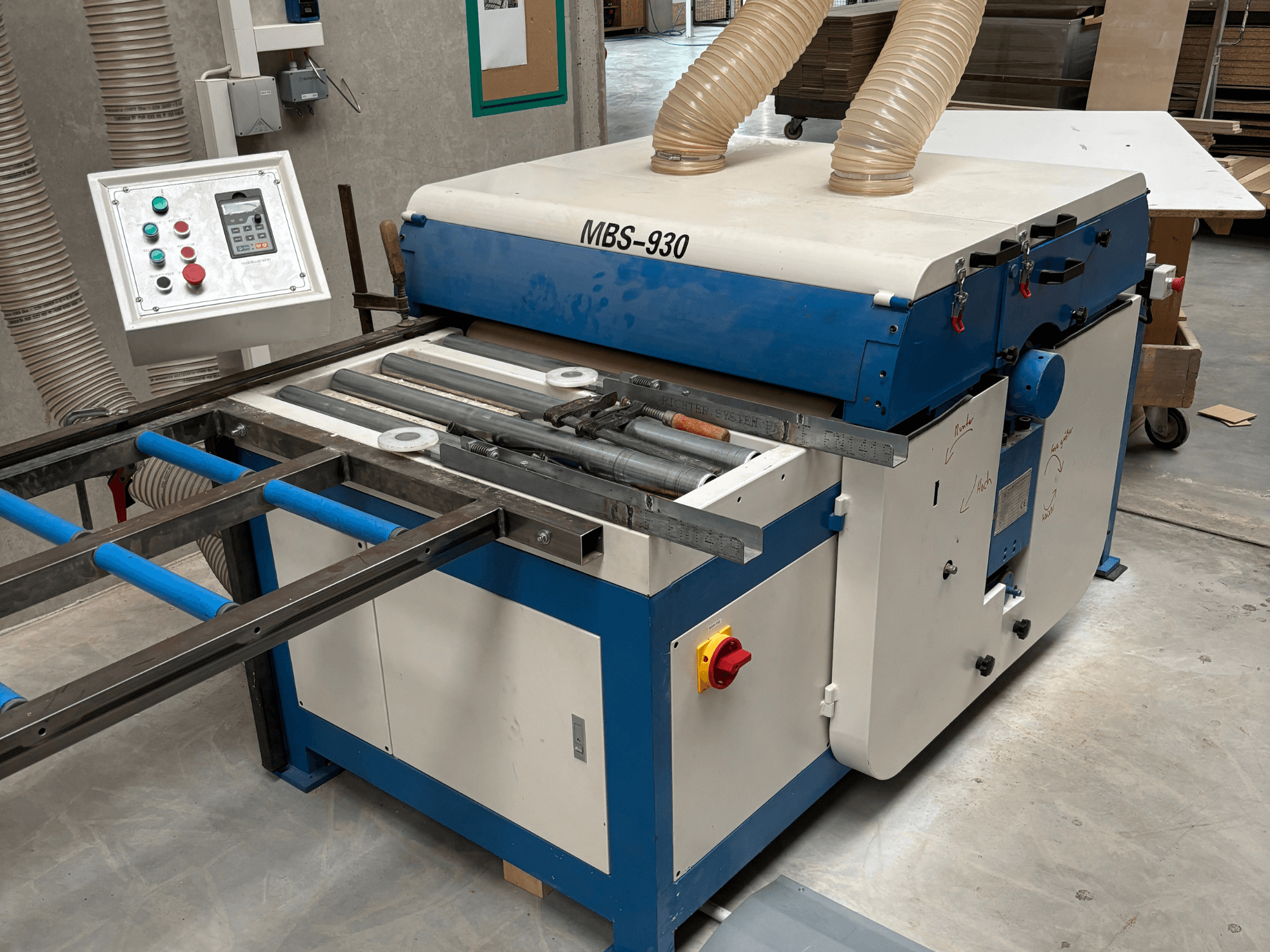 Máquina para trabajar la madera MBS-930 con panel de control y rodillos, vista desde el lateral, con mangueras de extracción de polvo.