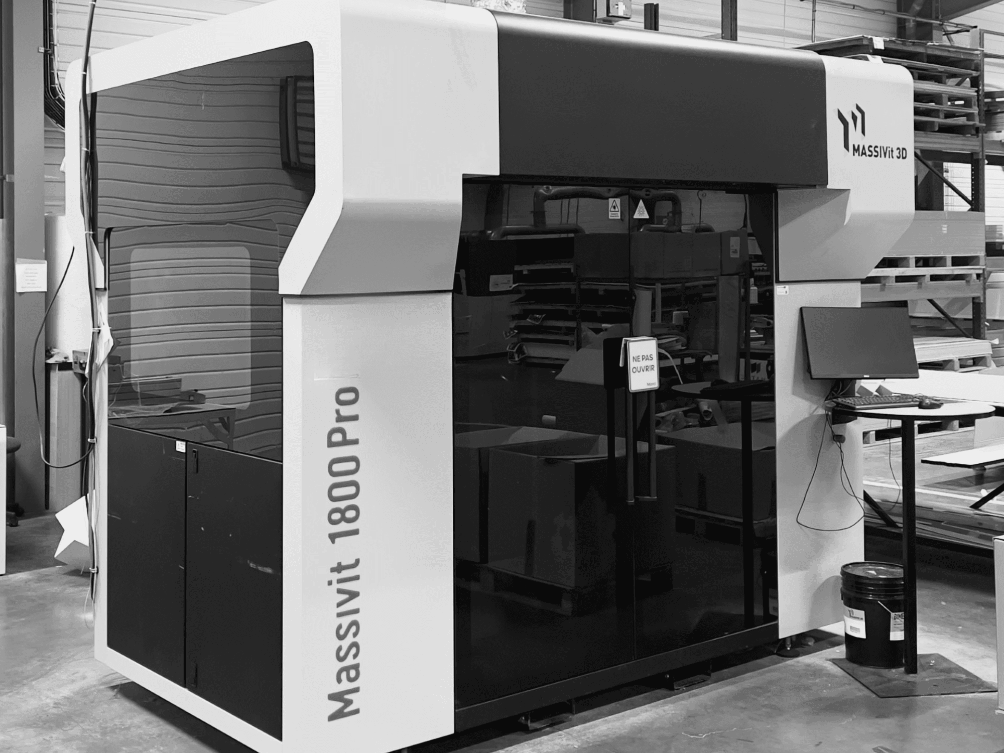 Impresora 3D de plástico MASSIVIT 1800 PRO en un taller, vista frontal, en la que se aprecian una estación de trabajo informática y un panel de control.