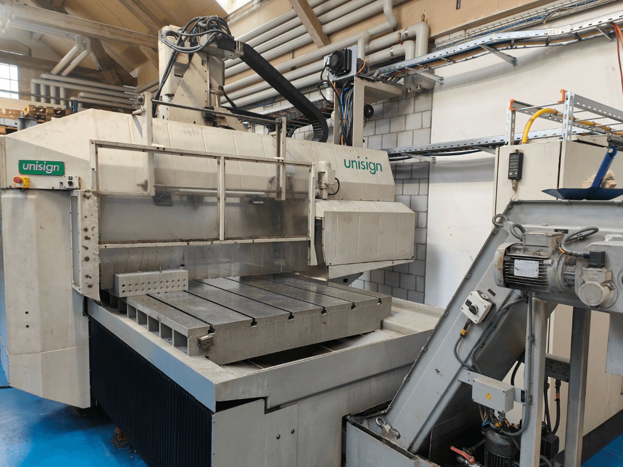 Máquina CNC Unisign en un taller, vista frontal, con una gran mesa, panel de control y elementos de diseño industrial.