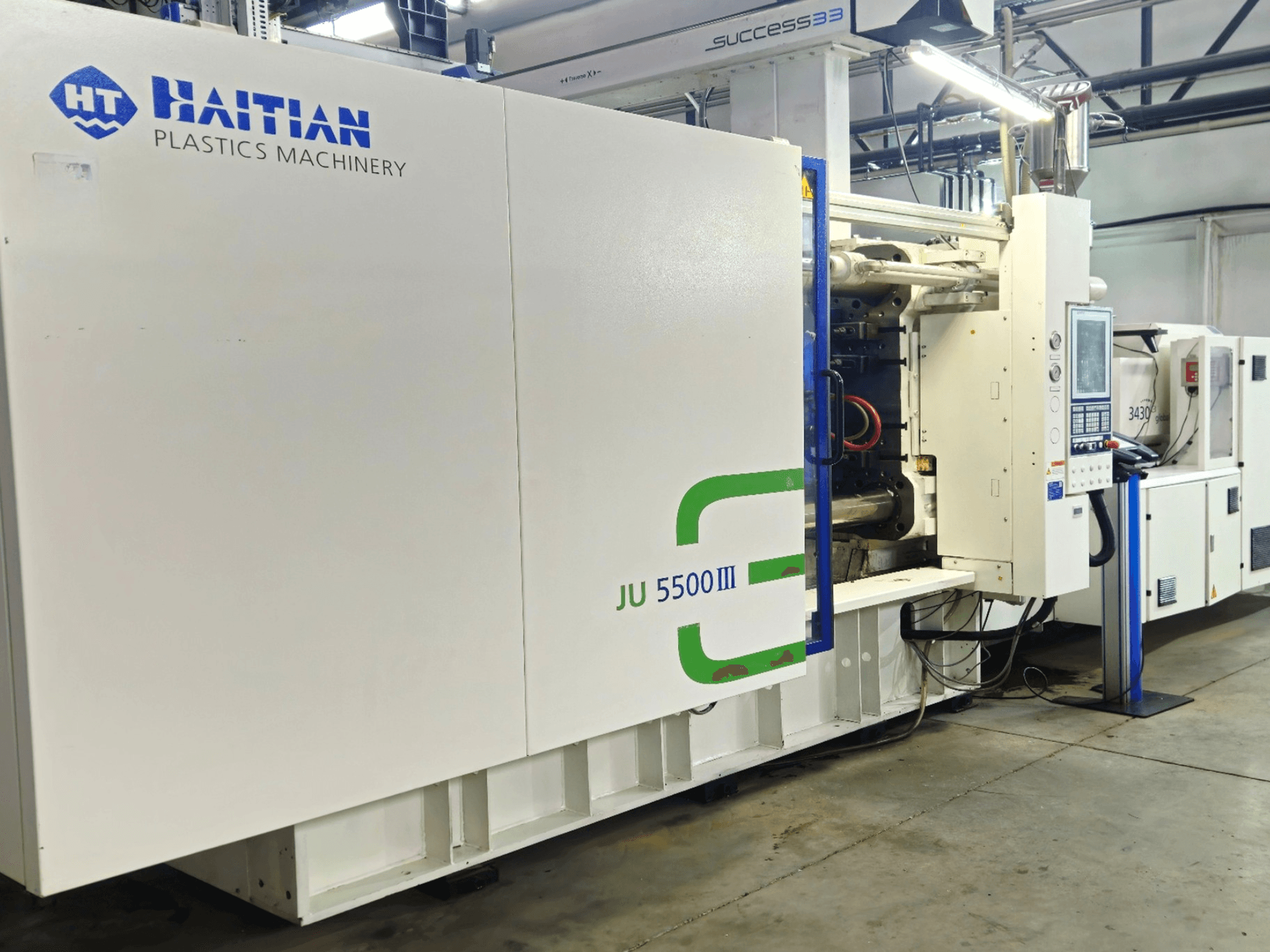 Maquinaria para plásticos JU 5500III de Haití en un entorno de fábrica, vista frontal que muestra el panel de control y el área de producción.