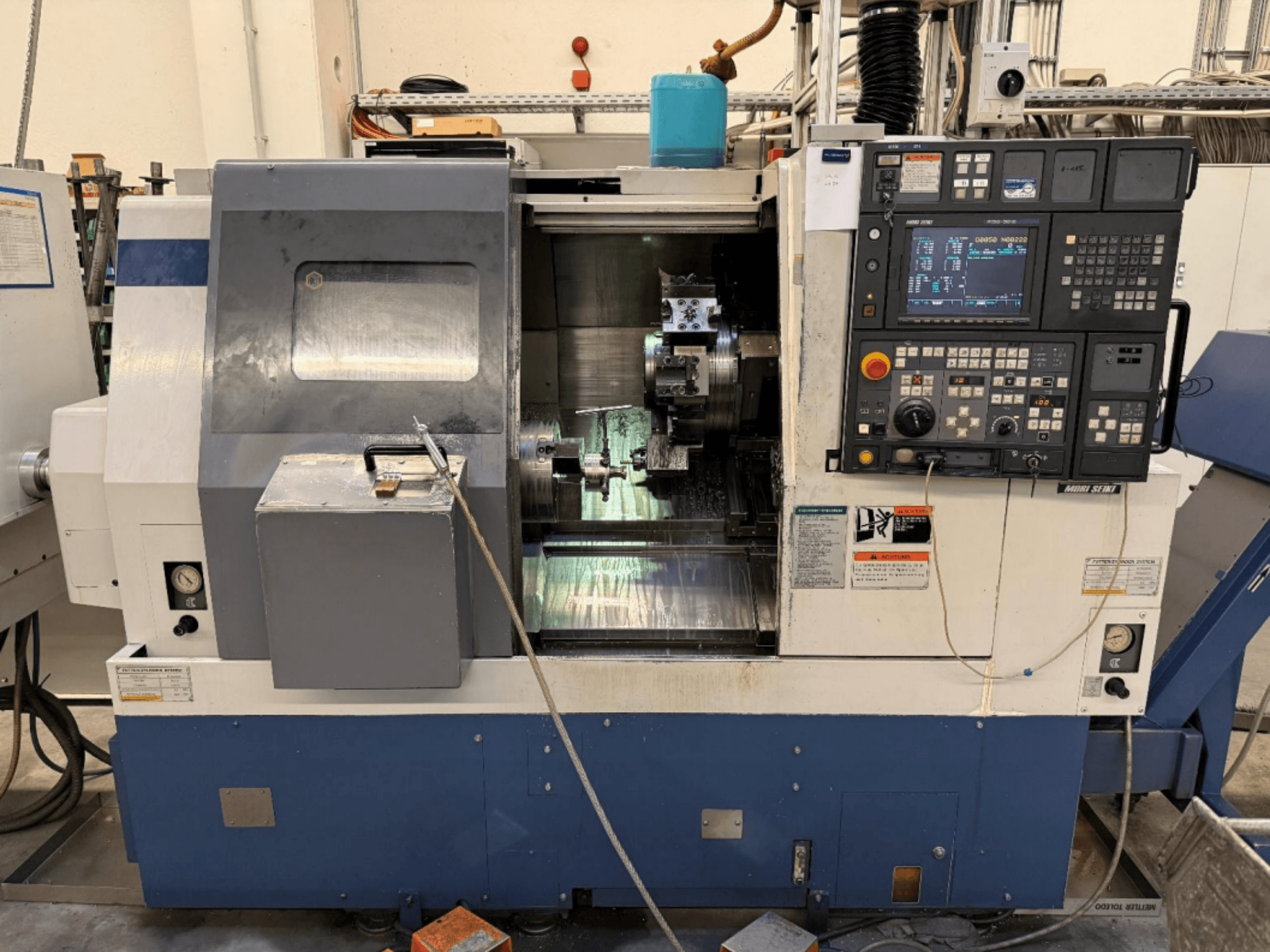 Centro de torneado y fresado MORI SEIKI SL-250ASMC, vista frontal en la que se aprecian el panel de control y el mandril de sujeción de la pieza en funcionamiento.