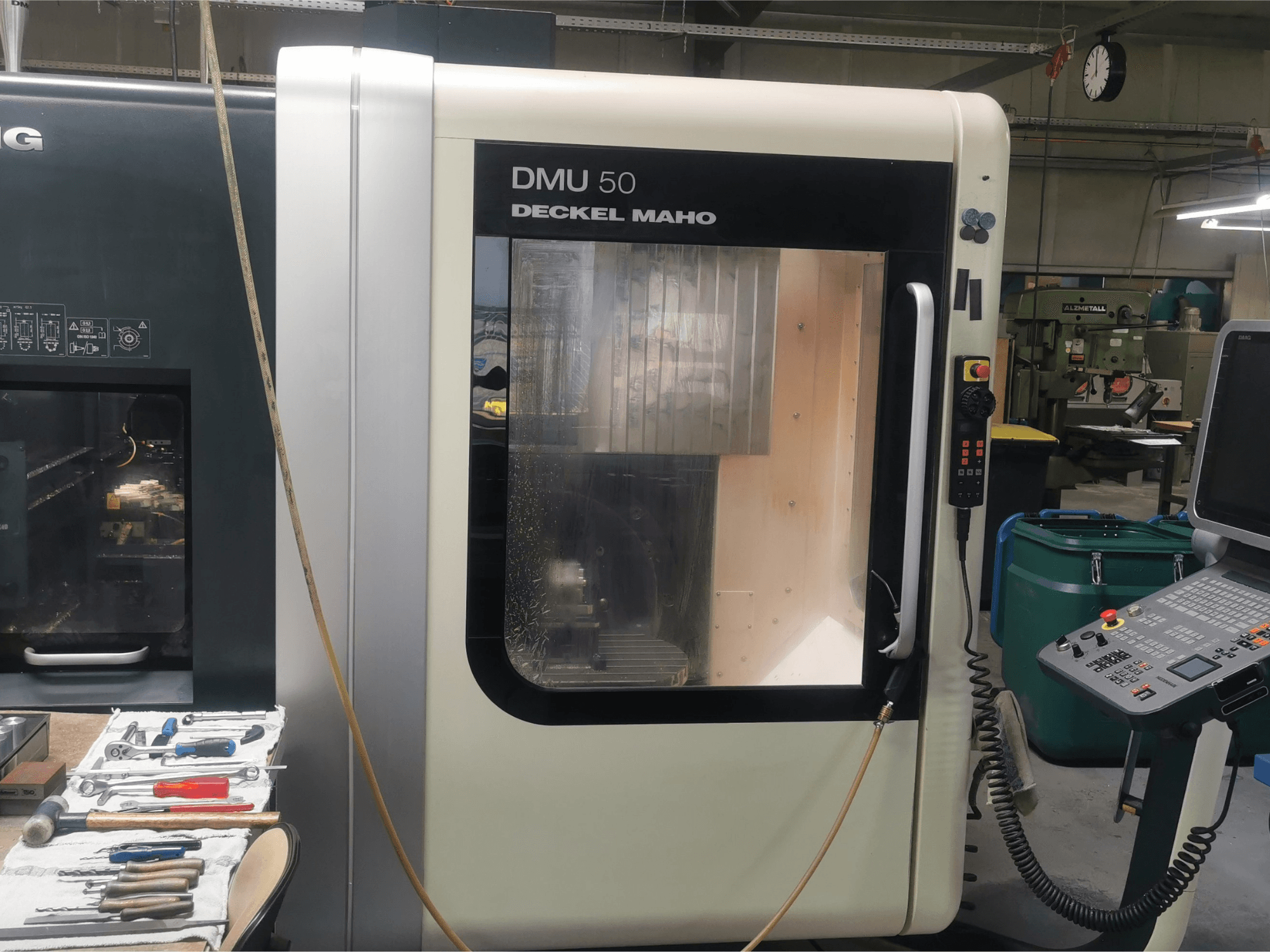 Máquina CNC DMU 50 deckel maho vista de frente, mostrando su panel de control y la puerta transparente. Las herramientas están cerca.