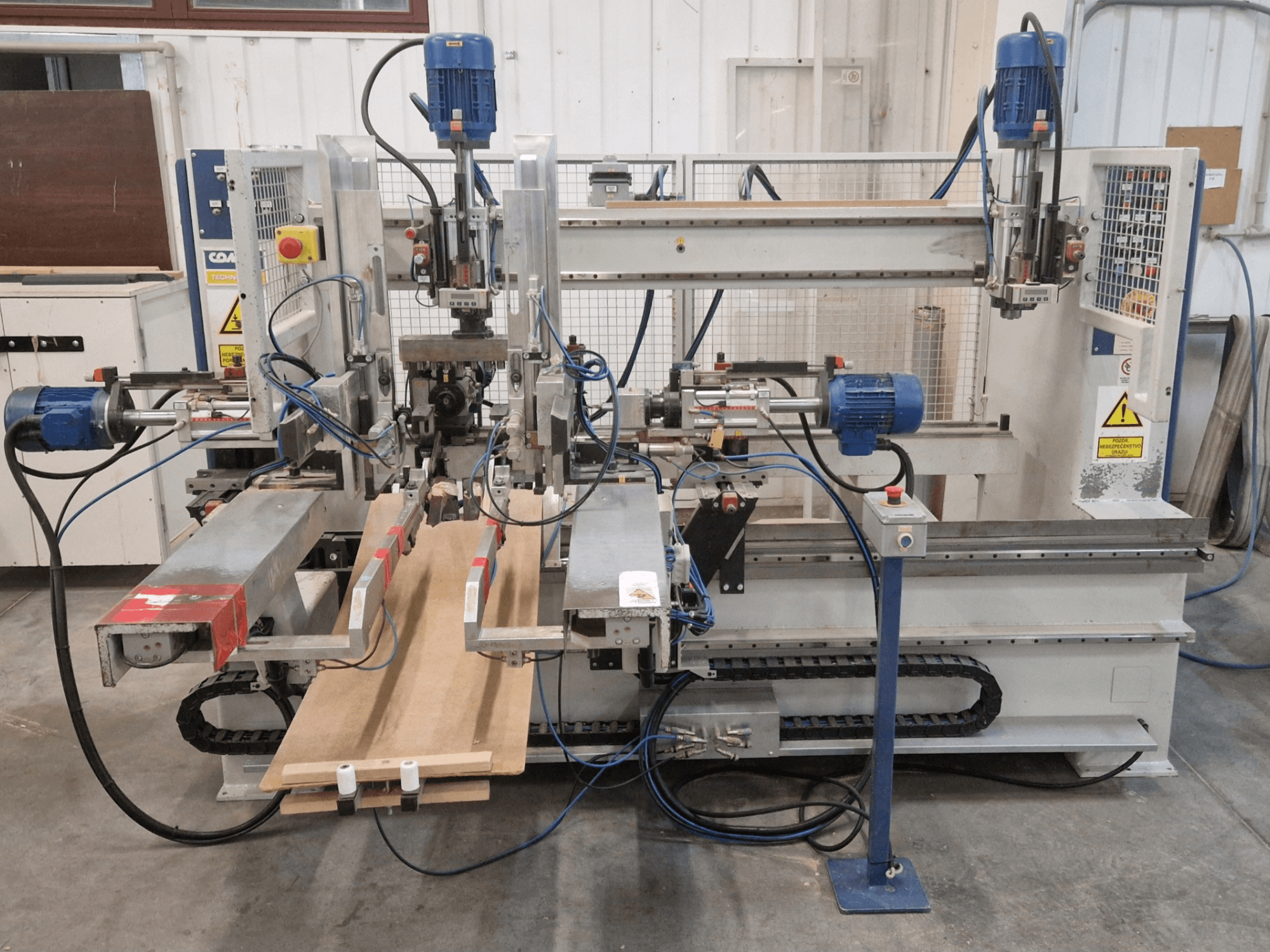 Vista frontal de la taladradora multihusillo COMEC FMOV 1500, mostrando los dos husillos, el panel de control y la pieza de madera en funcionamiento.