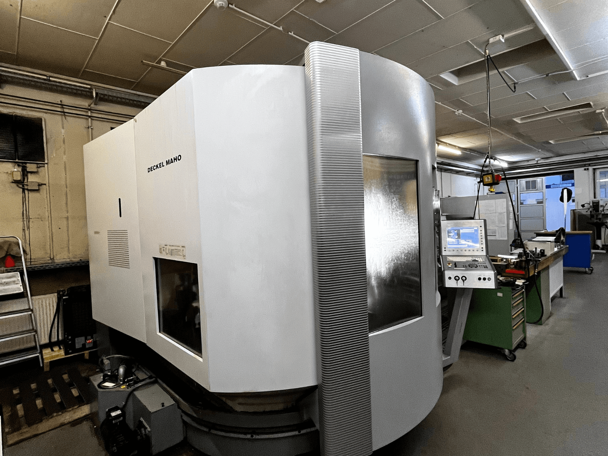 Máquina CNC Deckel Maho, vista frontal, exterior blanco, panel de control visible, entorno de taller.