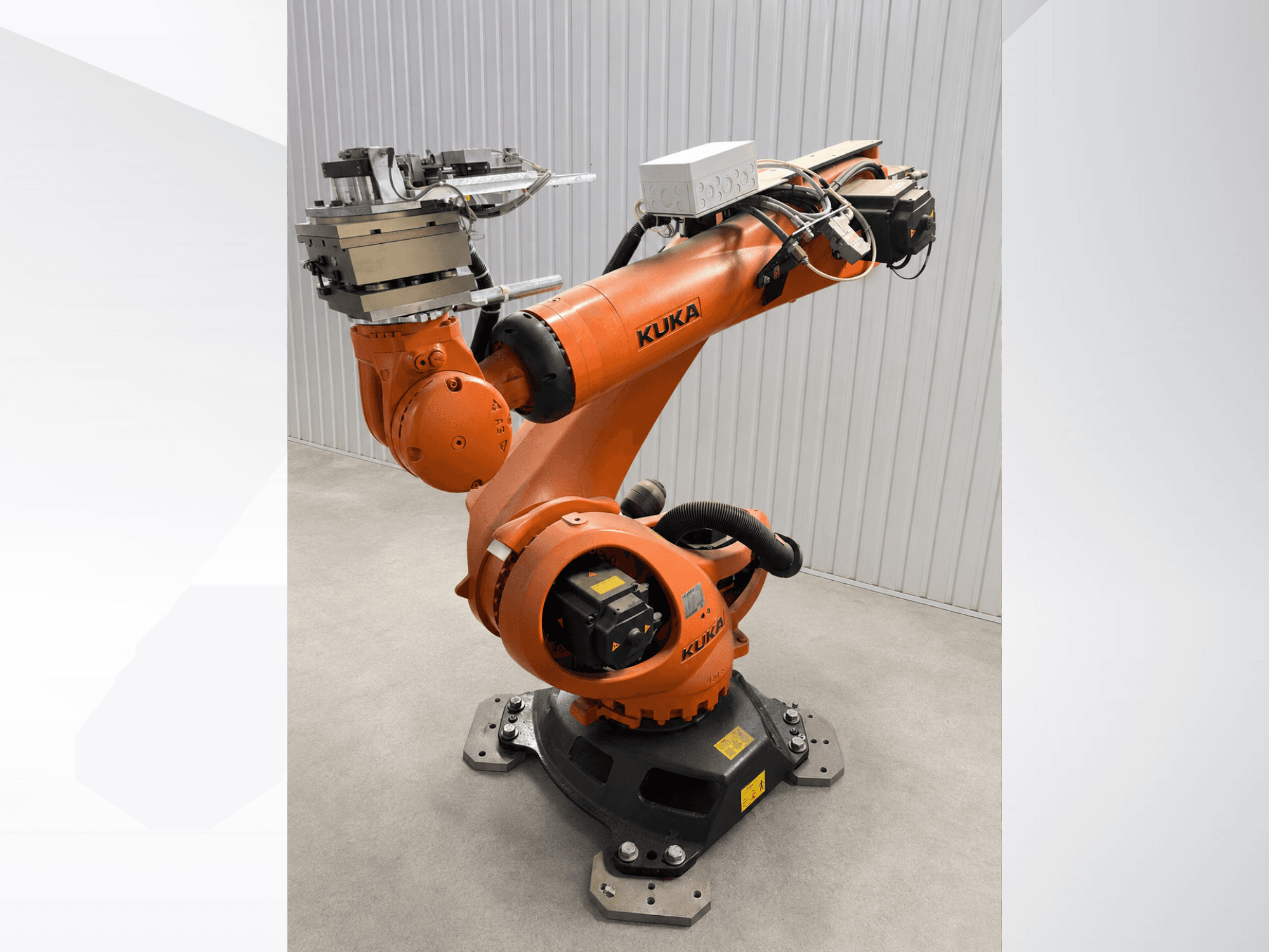 Brazo robótico adicional KUKA KR 90 R3100 en color naranja, vista lateral, en la que se aprecian las articulaciones, el controlador y el accesorio de la herramienta en el efector final.