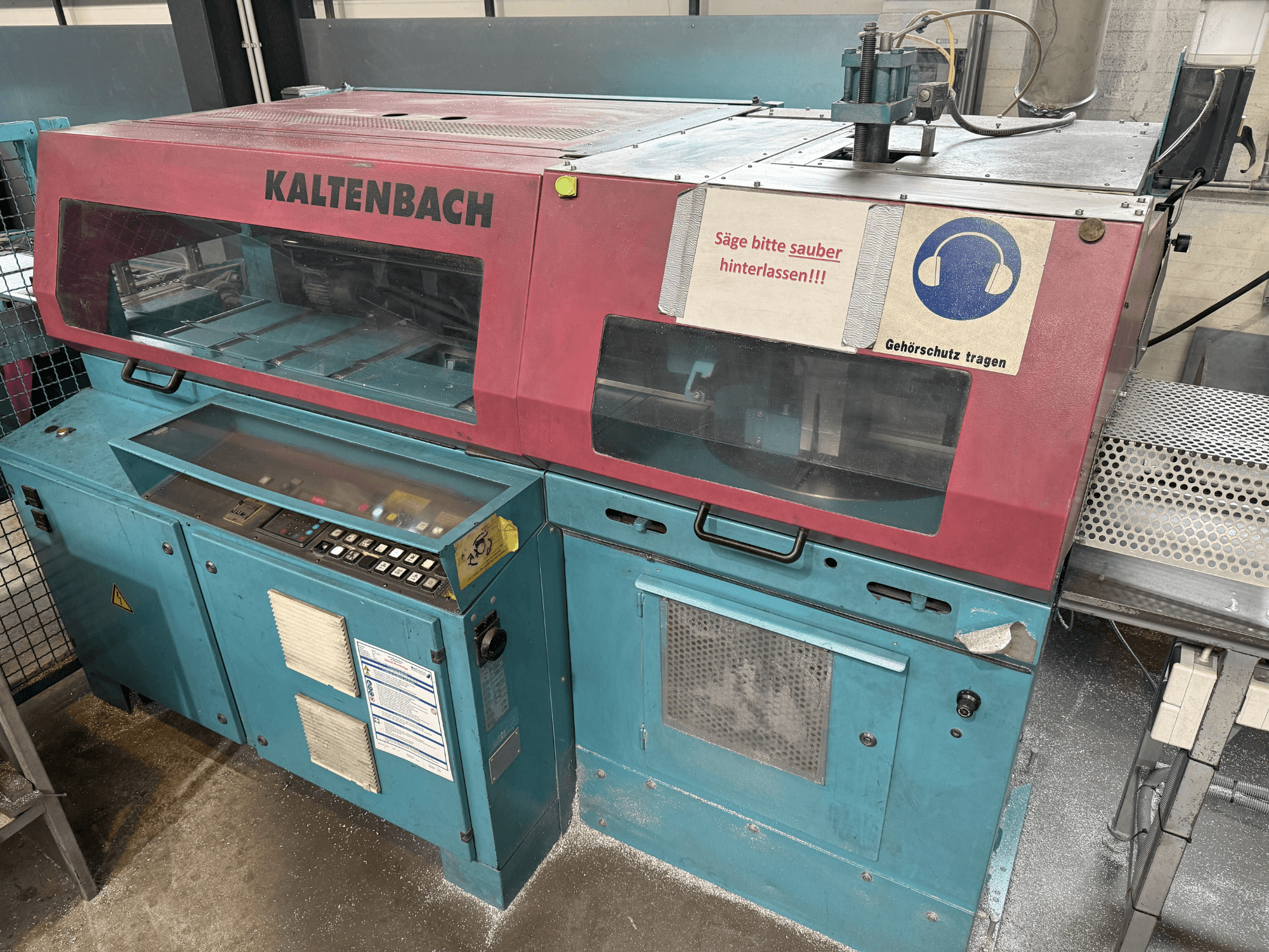 Máquina de corte industrial KALTENBACH, vista frontal, con panel de control y señal de seguridad para protección auditiva.