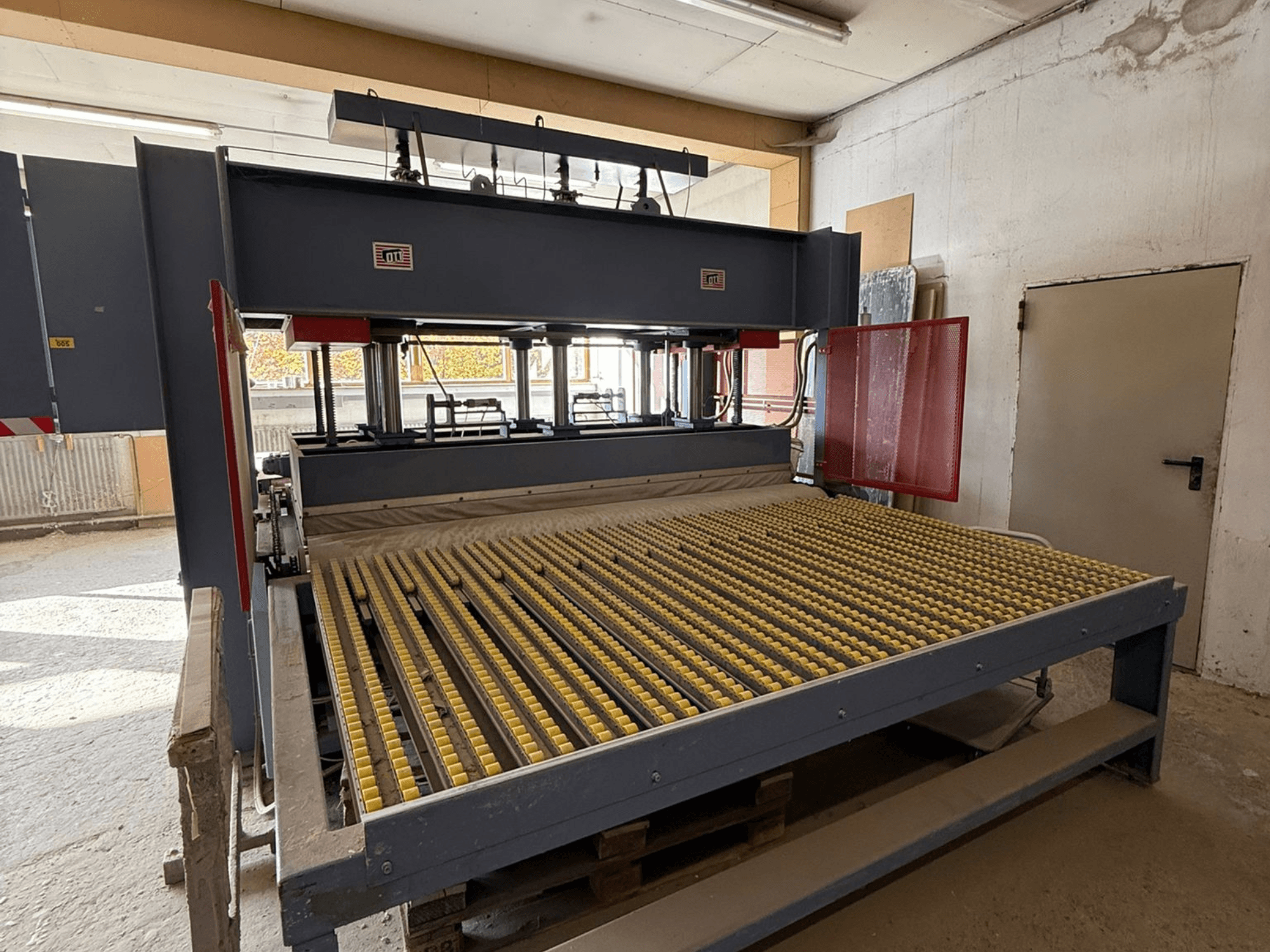 Máquina industrial con rodillos amarillos, vista frontal, logotipo de la marca visible, utilizada para procesar materiales en un taller.