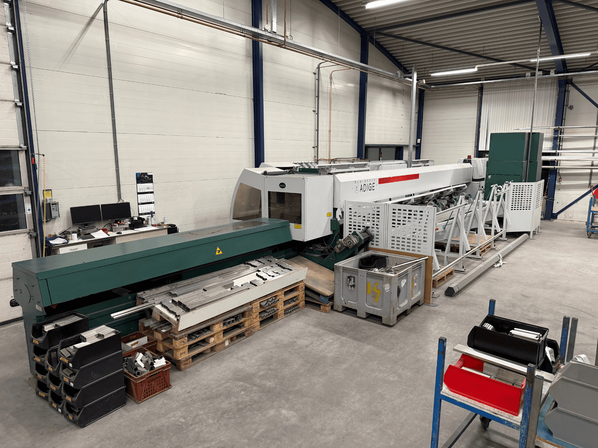 Máquina de corte por láser de CO₂ BLM Adige LT702 en un taller; vista lateral en la que se aprecian los componentes metálicos y el desorden del espacio de trabajo.
