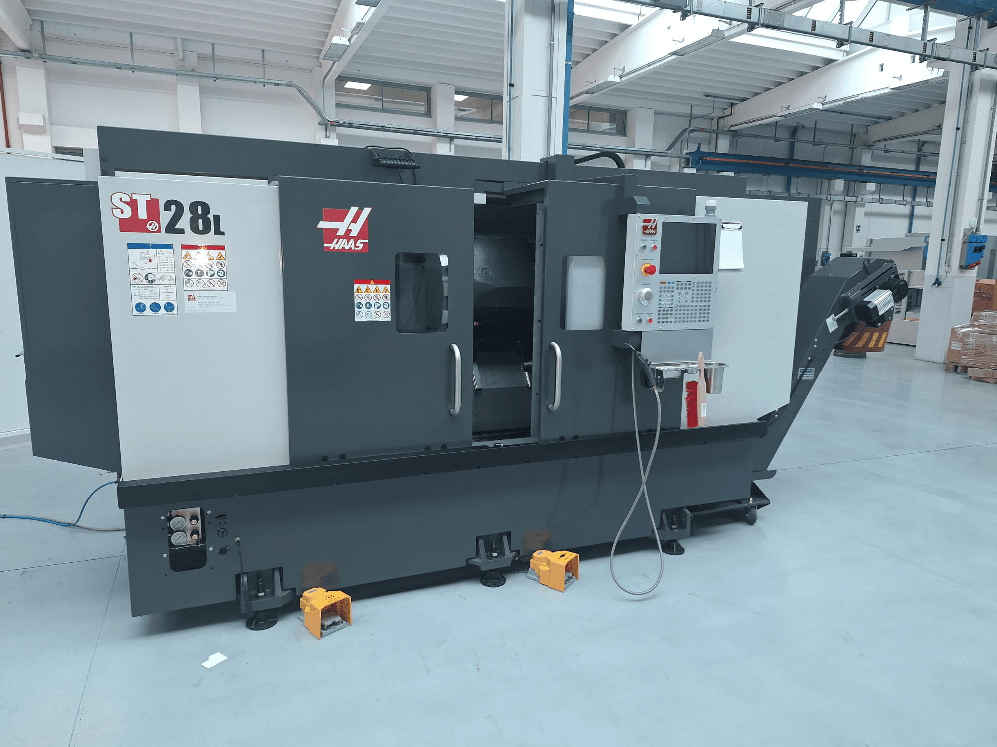 Vista lateral del torno horizontal Haas ST-28L, en la que se aprecian el panel de control, los botones de funcionamiento y las etiquetas de seguridad.