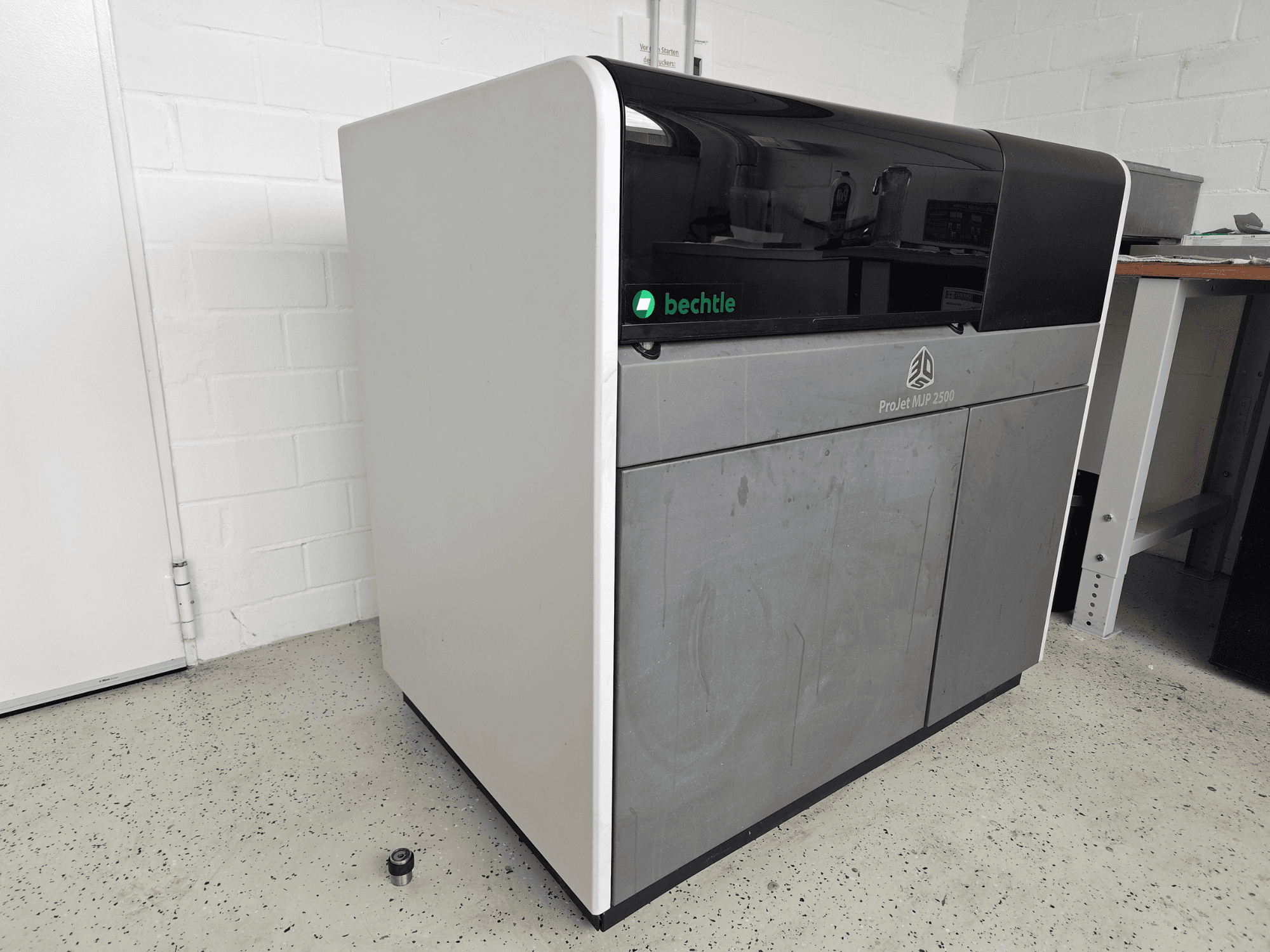 Impresora de plástico ProJet MJP 2500 Plus de 3D Systems vista de frente; presenta un diseño elegante con la parte superior oscura y el cuerpo claro.