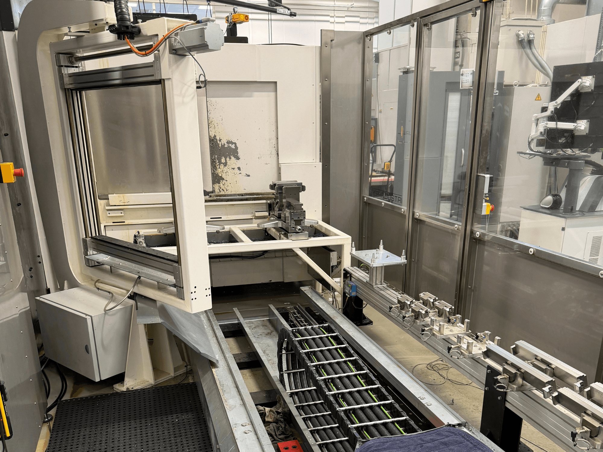 Estación de trabajo industrial automatizada que muestra un brazo robótico, un sistema de raíles y un panel de control en una vista lateral.