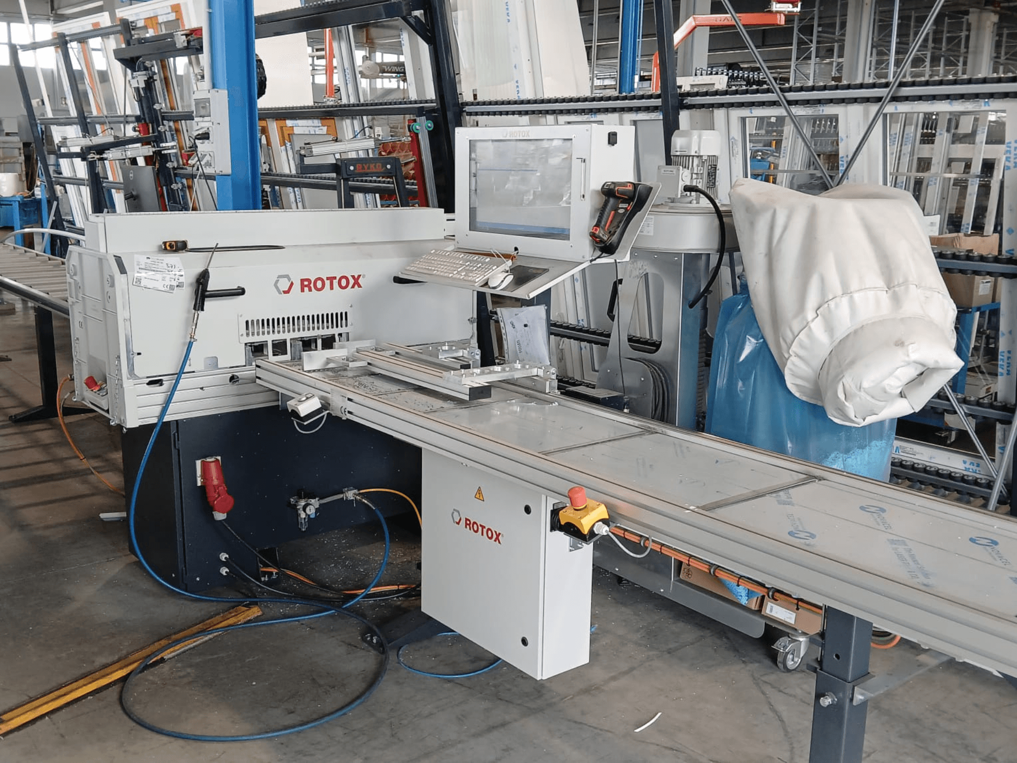 Vista frontal de una máquina de procesamiento de plástico Rotox GLA401 con panel de control, cinta transportadora y mangueras visibles en un entorno industrial.