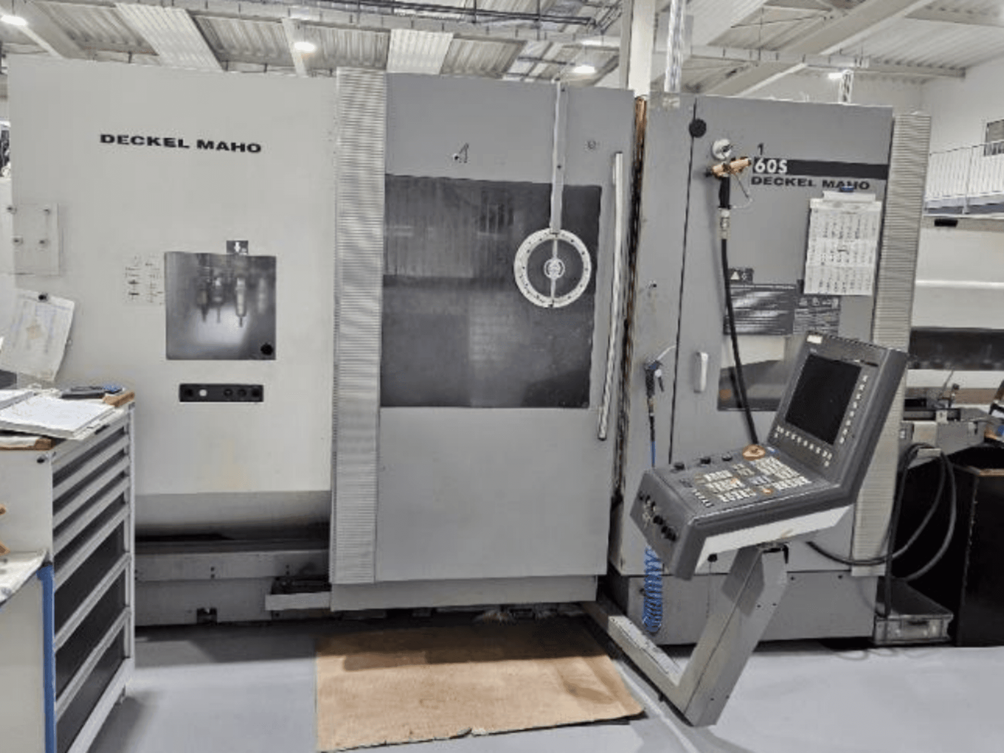 Vista frontal de una máquina CNC DECKEL MAHO 60S con panel de control, herramientas visibles, en un taller.