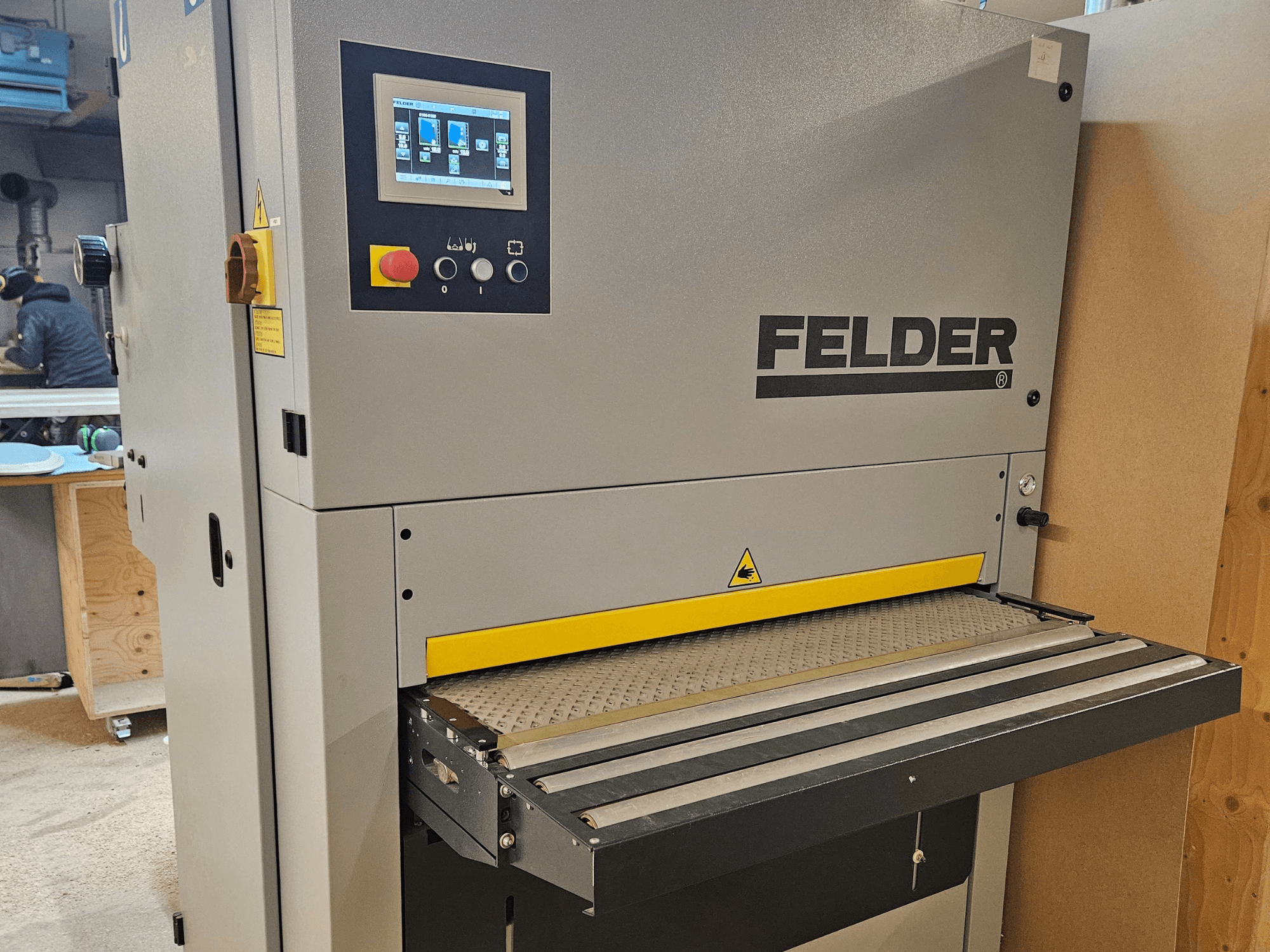 Máquina para trabajar la madera FELDER en vista frontal, con panel de control digital y mesa de alimentación amarilla con advertencias de seguridad.