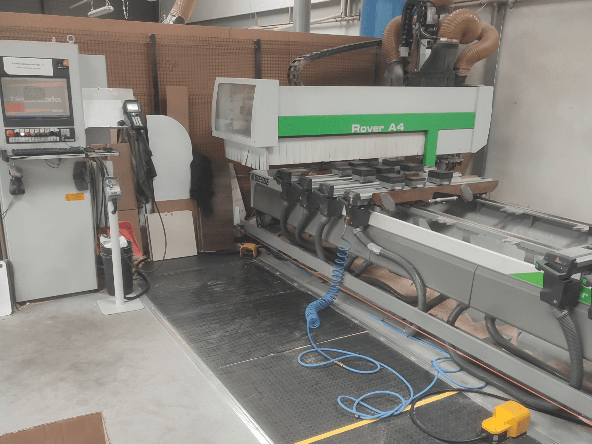 Centro de mecanizado de madera CNC BIESSE Rover A4 en vista lateral, en el que se aprecian el panel de control, los dispositivos de sujeción por vacío y el sistema de extracción de polvo.