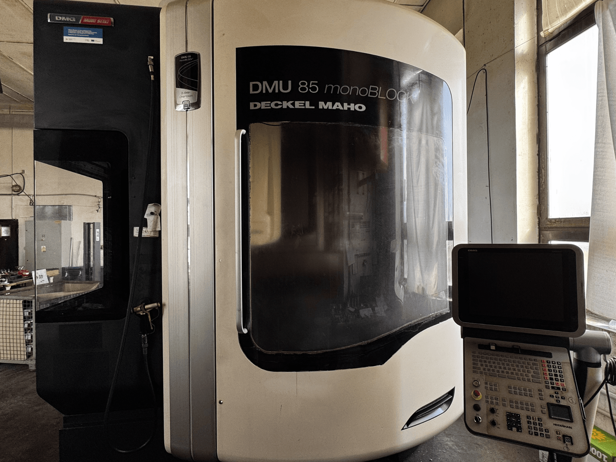 Centro de mecanizado vertical DMG MORI DMU 85 monoBLOCK, vista frontal con panel de control y gran ventana de visualización.