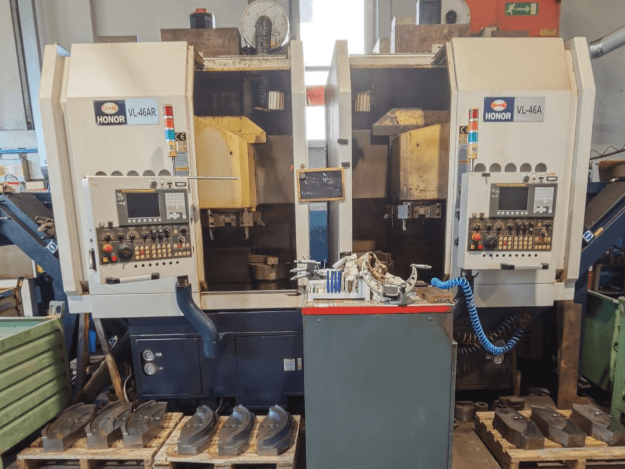 Vista frontal del torno vertical HONOR SEIKI VL 46A, en la que se aprecian el panel de control y los componentes circundantes sobre palés de madera.