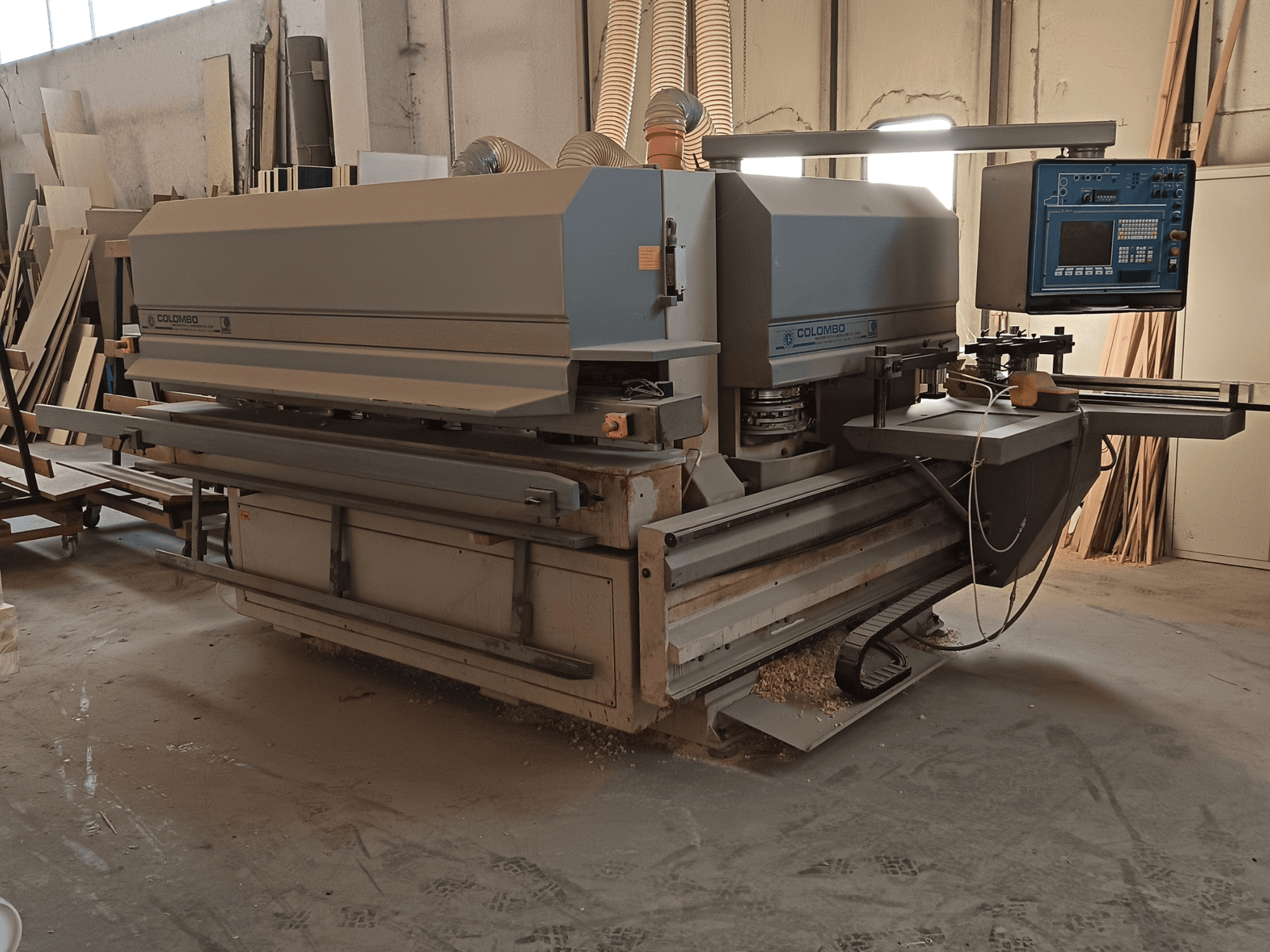 Máquina para trabajar la madera Colombo, vista lateral, mostrando el panel de control, las hojas de corte y la acumulación de serrín en el taller.