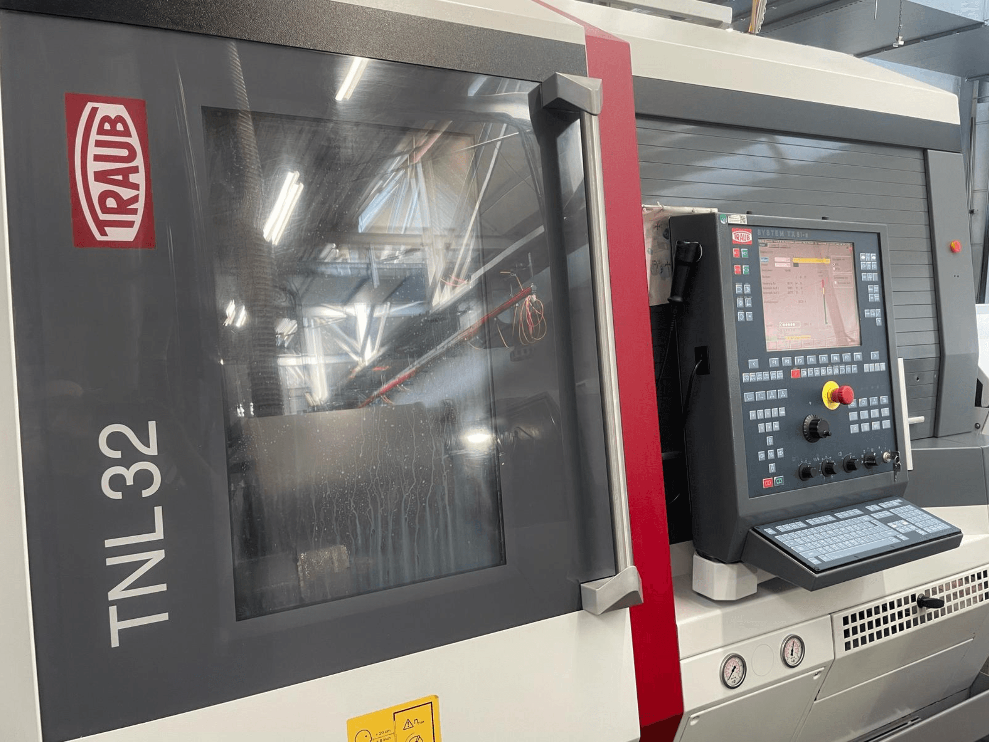 Vista frontal del torno CNC TNL32 de Traub, con panel de control con botones, pantalla de visualización y elegante carcasa metálica.