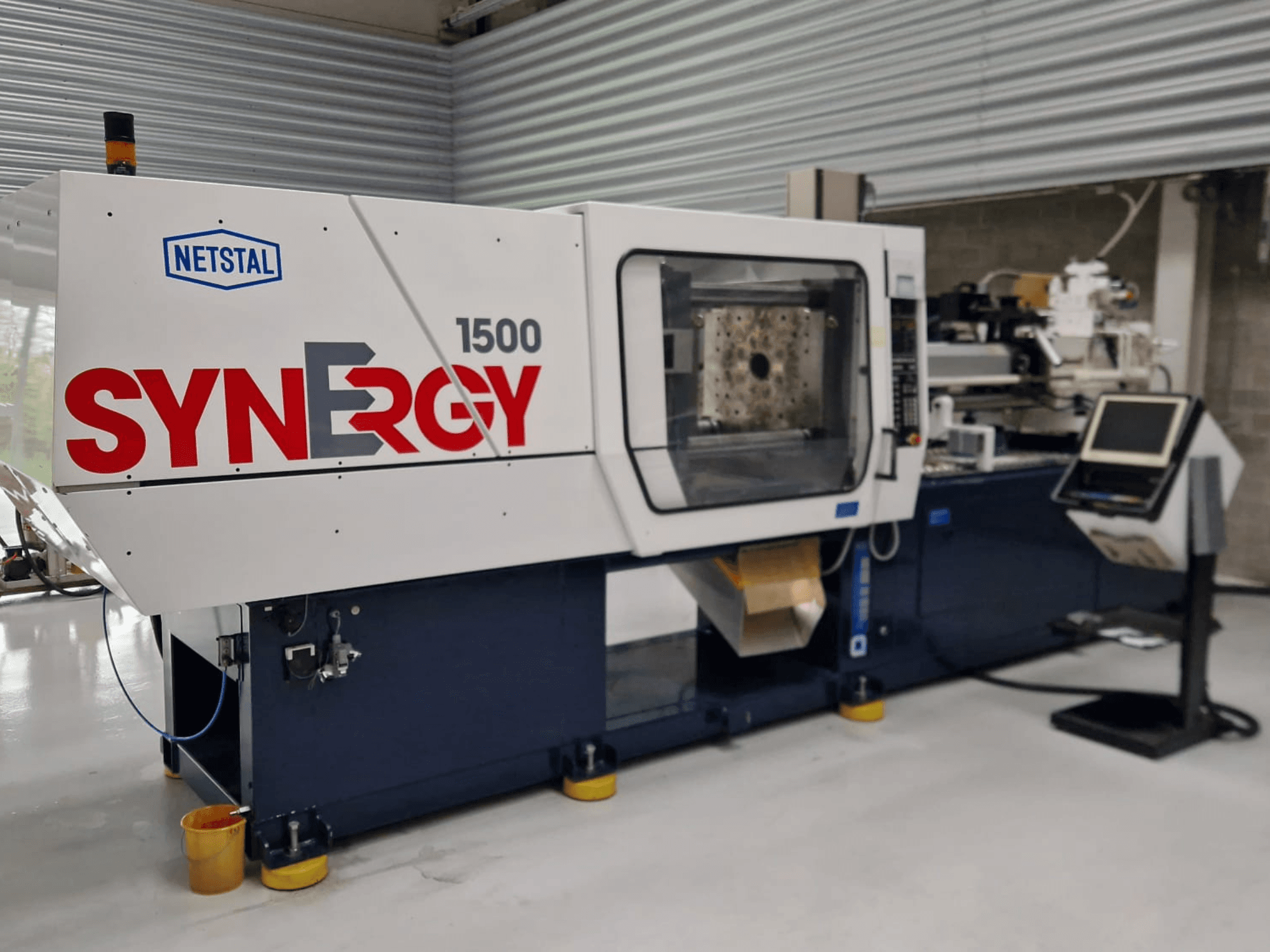 Máquina de moldeo por inyección hidráulica Netstal Synergy 1500-460, vista frontal, mostrando el panel de control y la zona de inyección abierta.