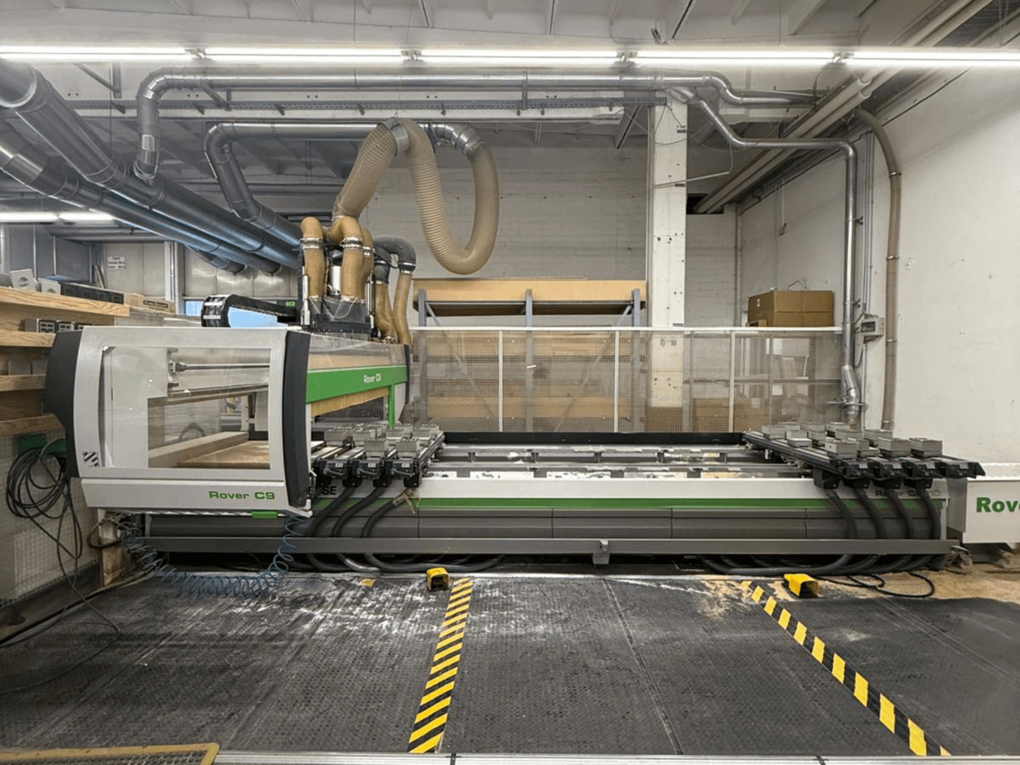 Máquina CNC Rover C9 en un taller, vista frontal, con múltiples cabezales de corte y sistema de extracción de polvo visible.