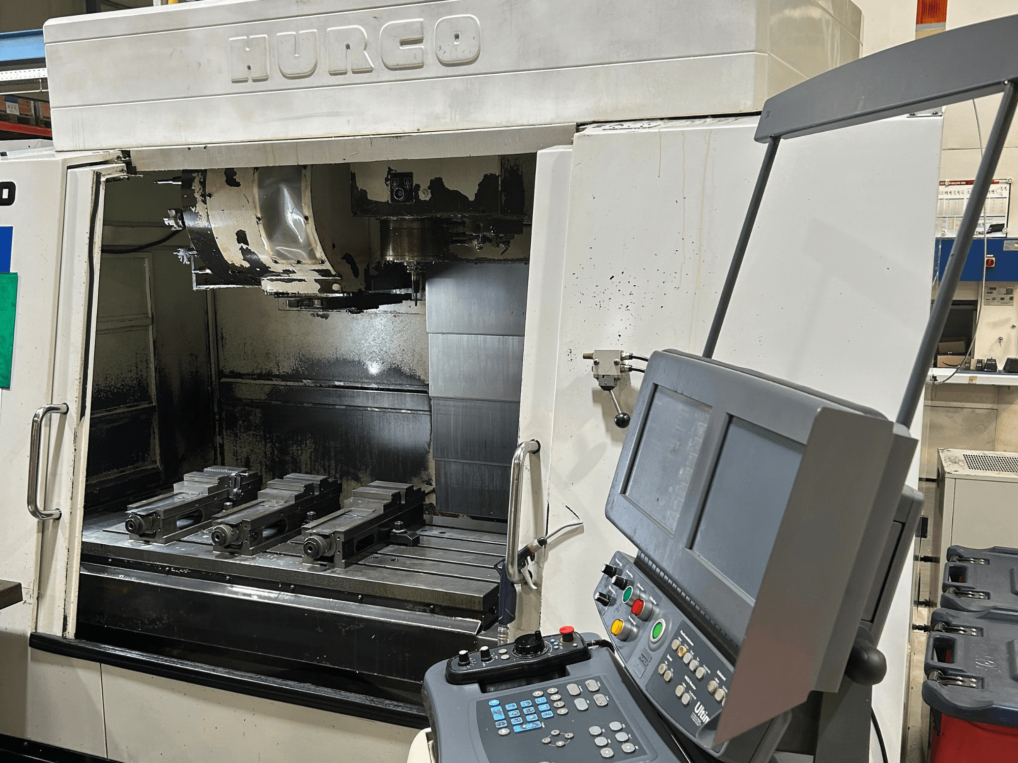 Fresadora CNC Hurco, vista frontal, con cuatro portaherramientas en la mesa y un panel de control con dos pantallas y botones.