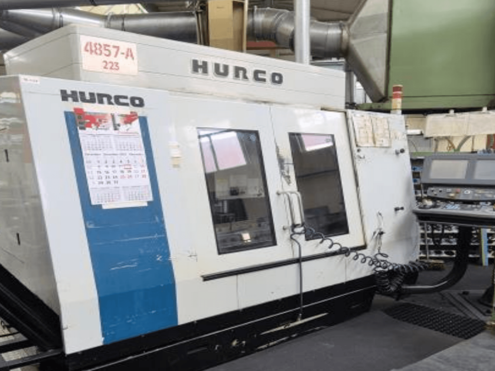 Centro de mecanizado vertical Hurco VMX 42 en vista frontal, con panel de control, calendario y detalles metálicos exteriores.