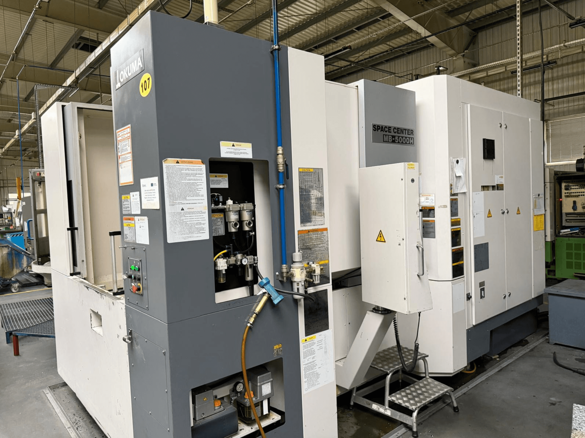 Centro de mecanizado horizontal Okuma MB 5000H, vista lateral que muestra el panel de control y los componentes de la maquinaria en un entorno de fábrica.