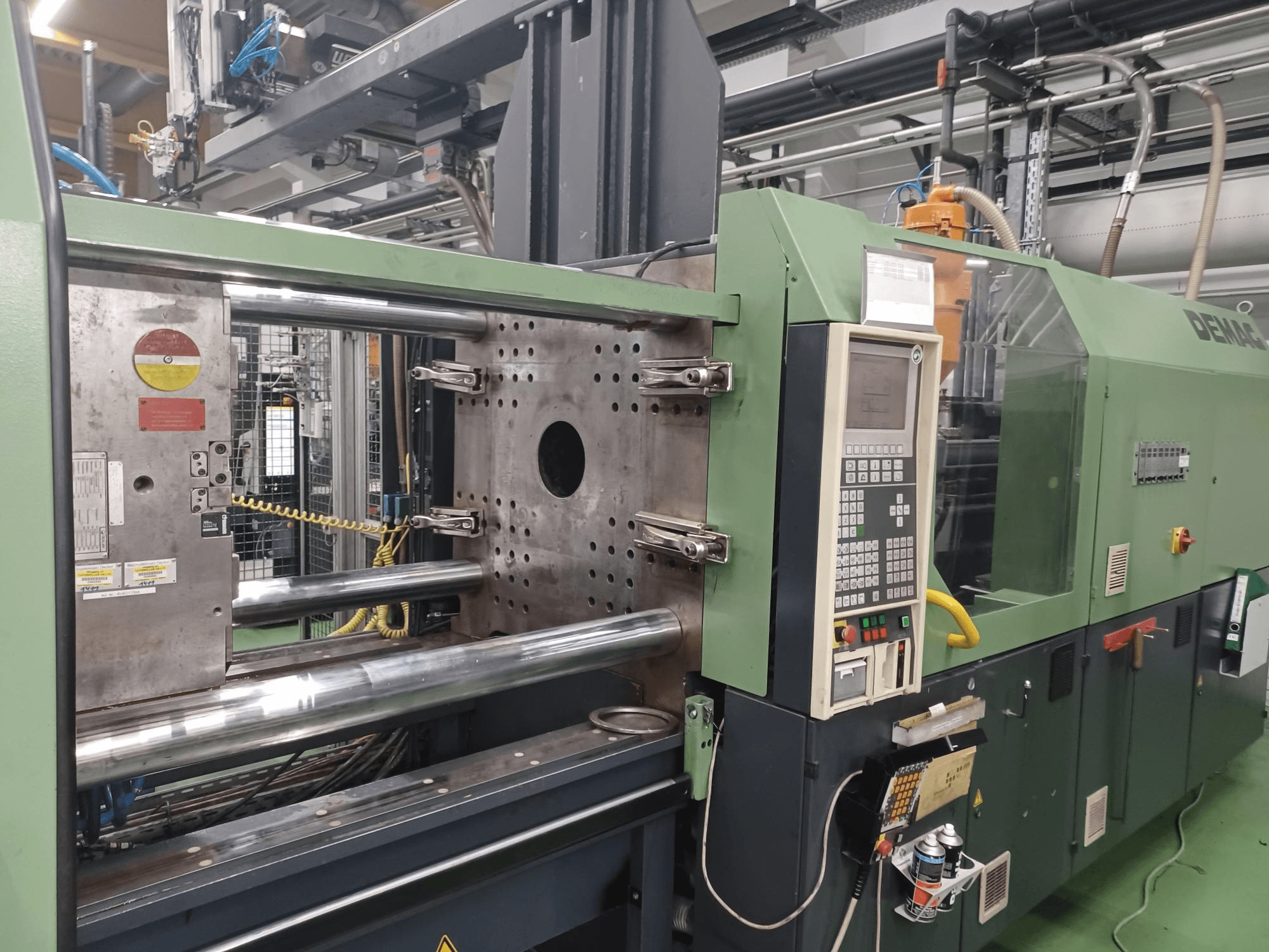 Máquina de moldeo por inyección Demag, vista frontal, con panel de control, cilindros hidráulicos metálicos y características de seguridad.