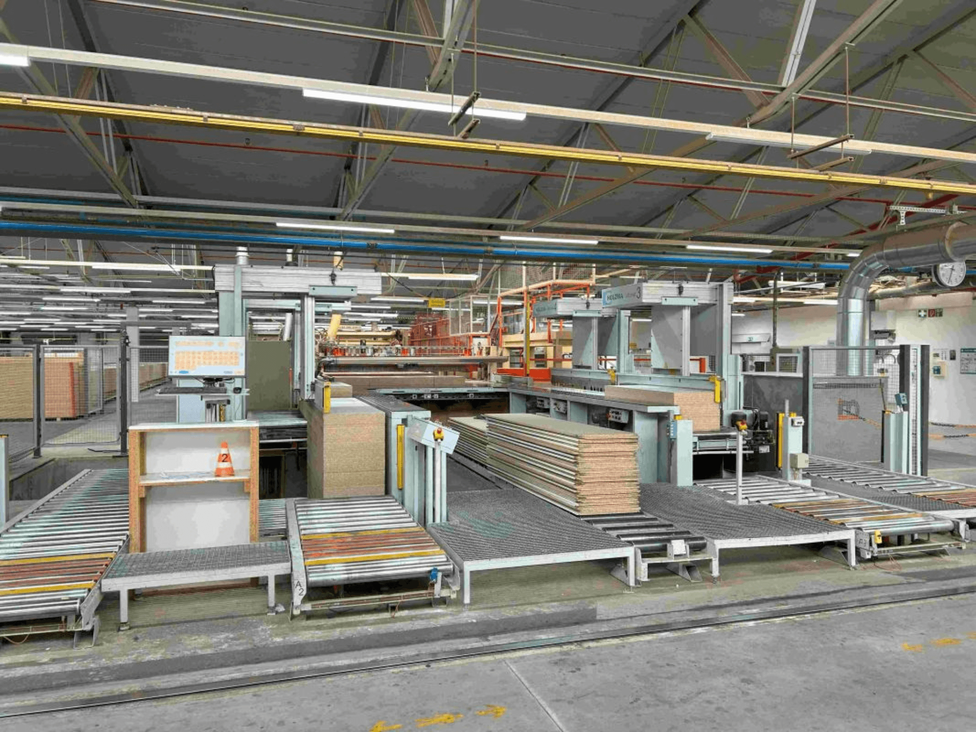 Interior de planta de fabricación mostrando líneas de montaje con paneles apilados y maquinaria, vista frontal, iluminación brillante, equipamiento moderno.