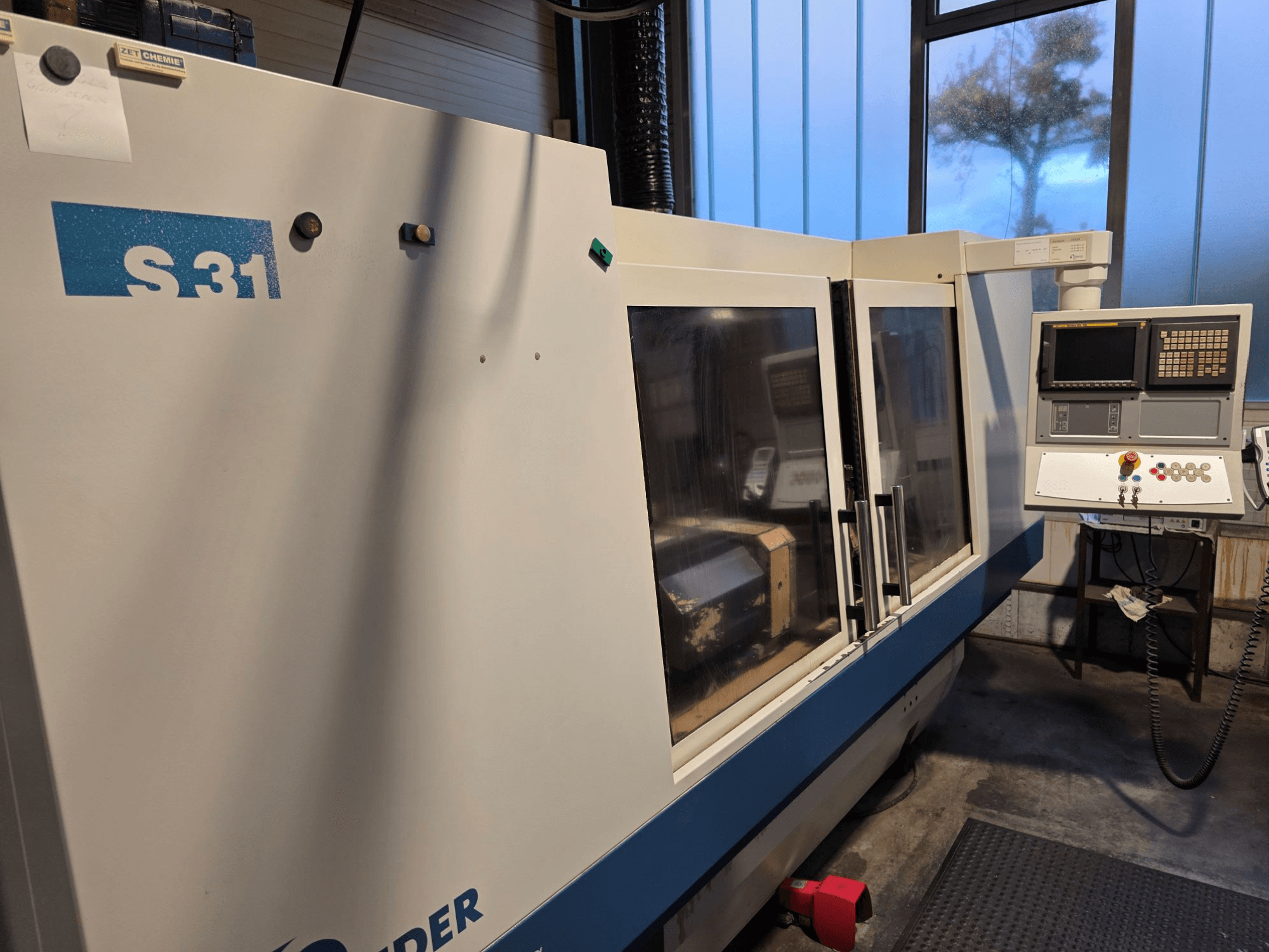 Rectificadora CNC S31, vista frontal, dispone de panel de control con pantalla y botones, gran puerta de cristal, entorno industrial.