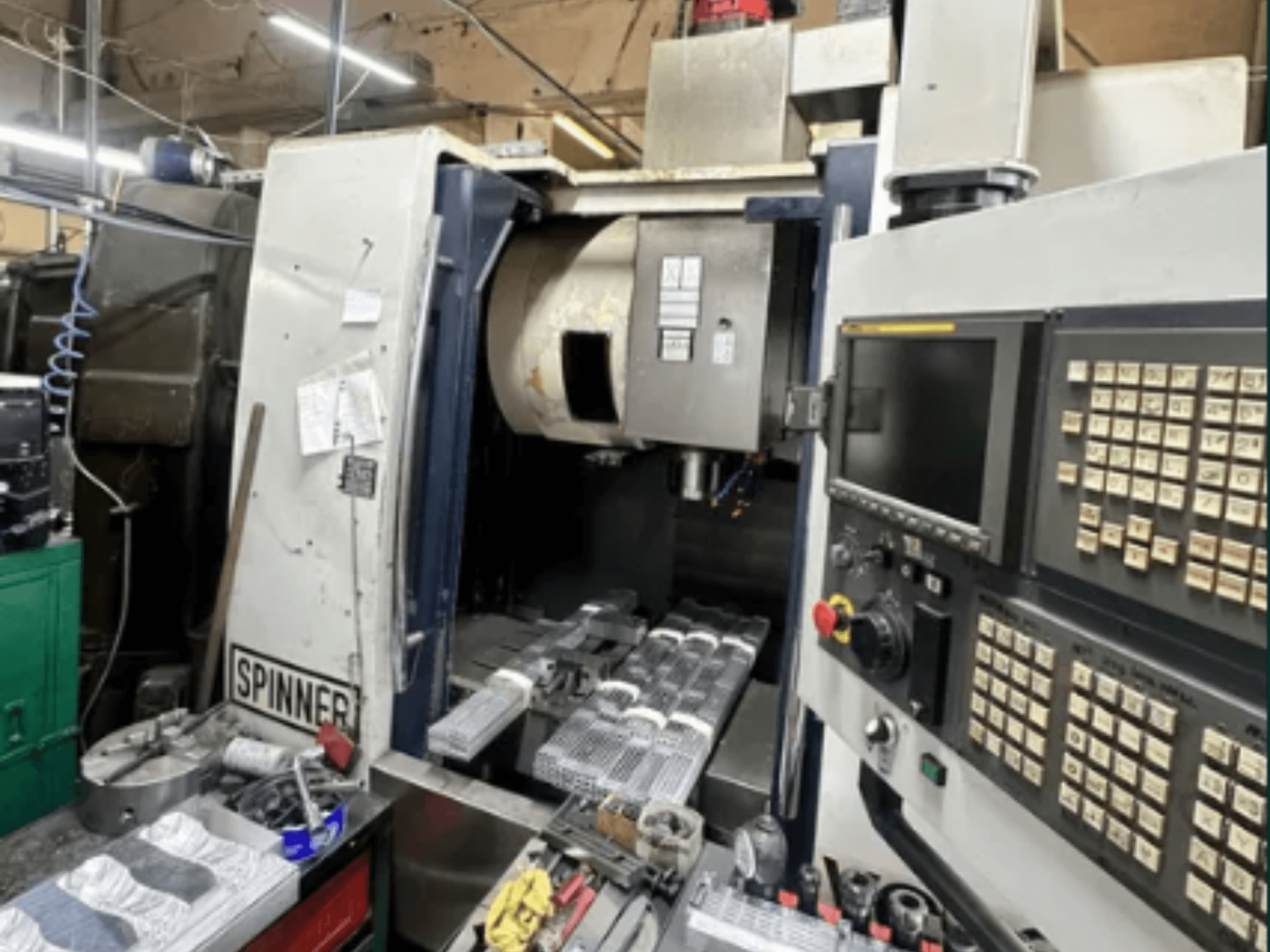 Máquina CNC de Spinner, vista frontal; cuenta con interfaz de pantalla táctil, herramientas en el espacio de trabajo y piezas mecanizadas listas para su procesamiento.